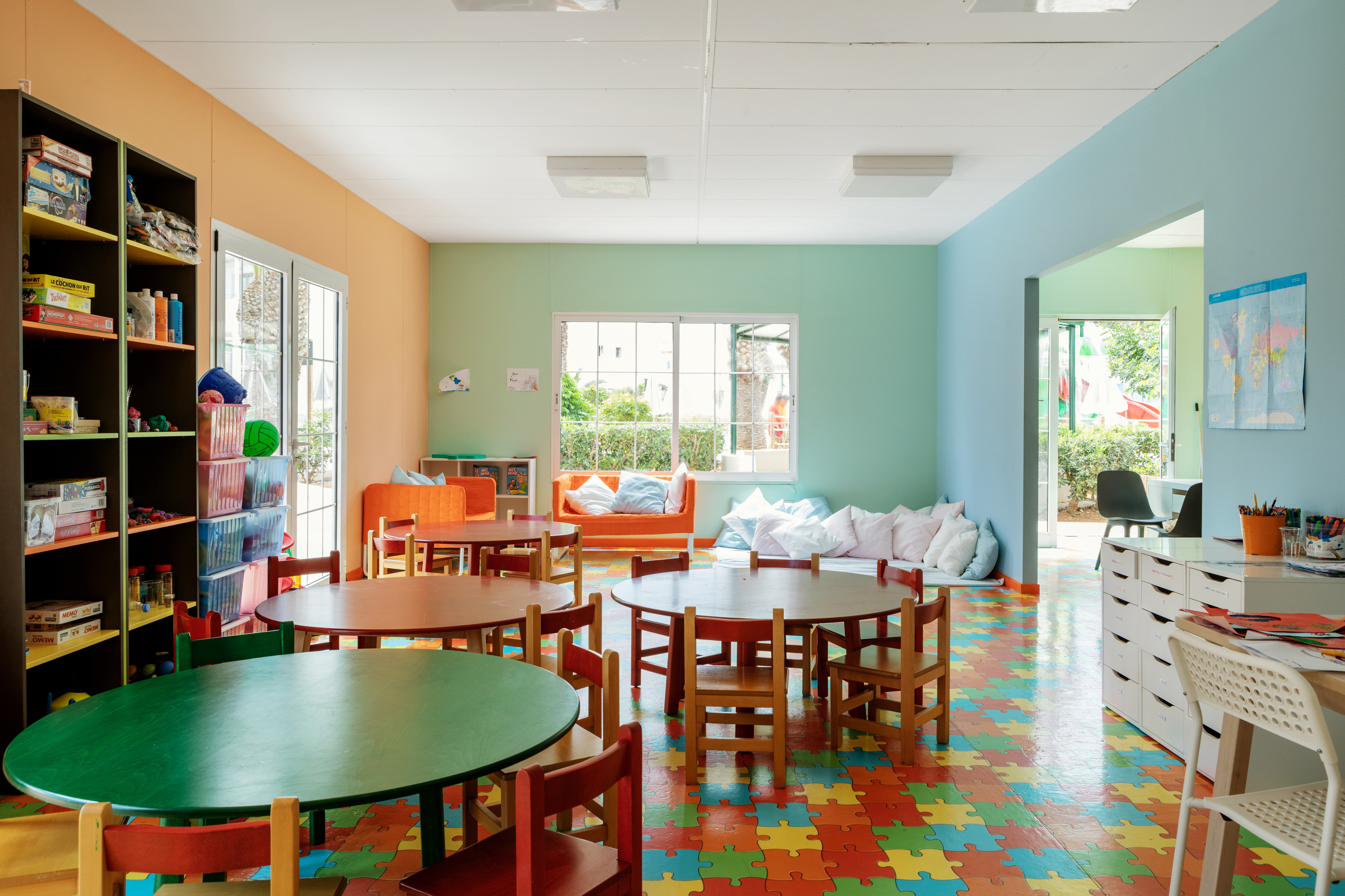Vibrant children's playroom with puzzle floor, small tables, chairs, and toys.