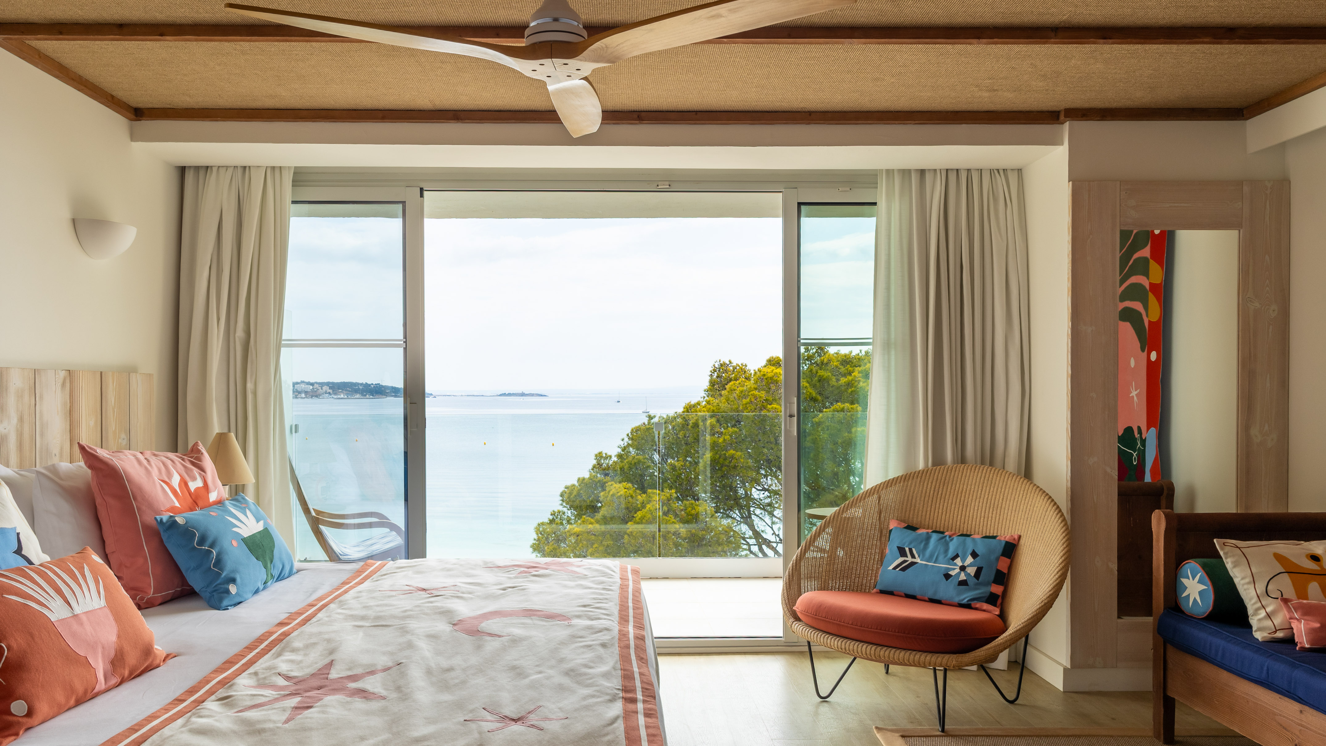 Hotel bedroom with ocean view balcony, coastal decor, and ceiling fan.