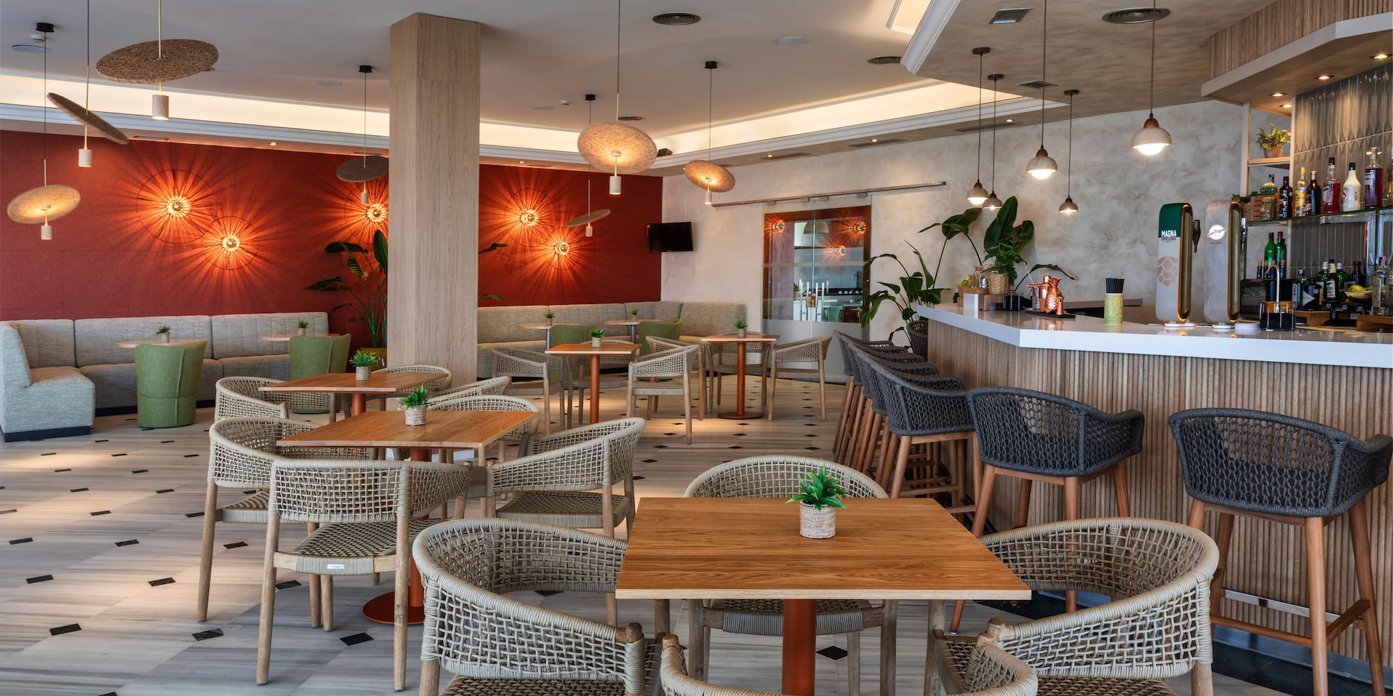 Comedor de hotel moderno con barra, mesas y sillas de mimbre.