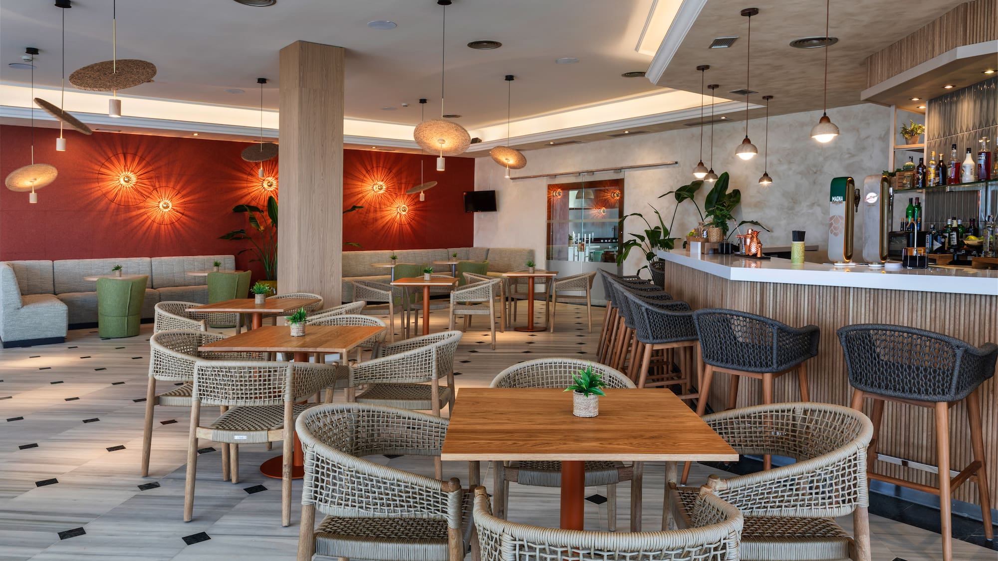 Comedor de hotel moderno con barra, mesas y sillas de mimbre.