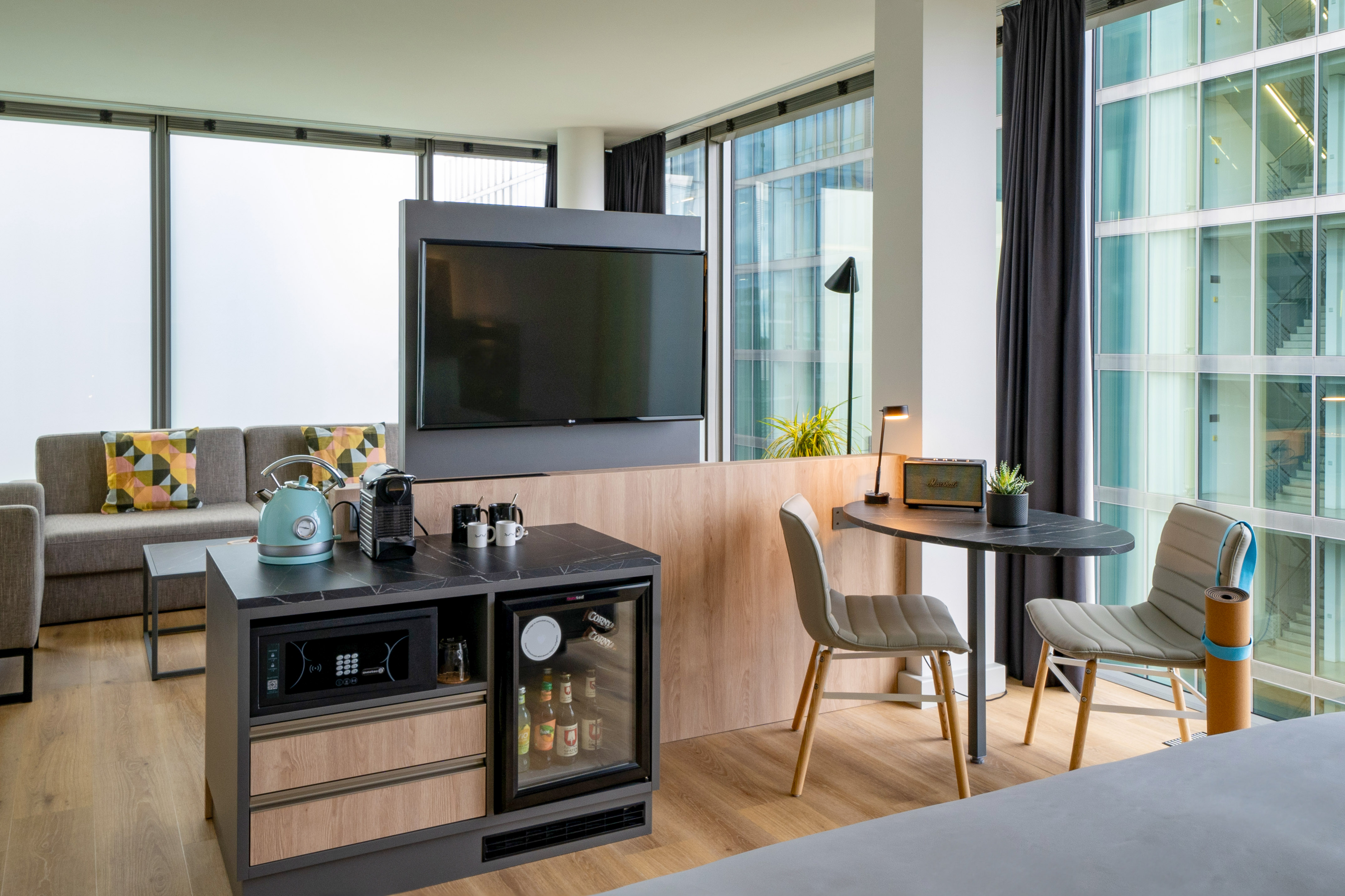 Modern hotel suite living area with kitchenette, TV, and city views.