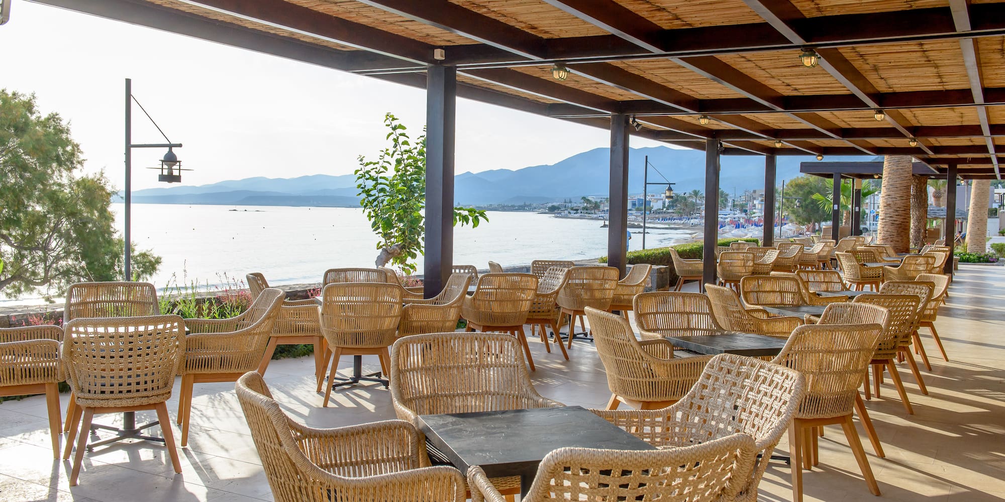 Beachfront restaurant patio with wicker chairs, sea view, and bamboo roof.