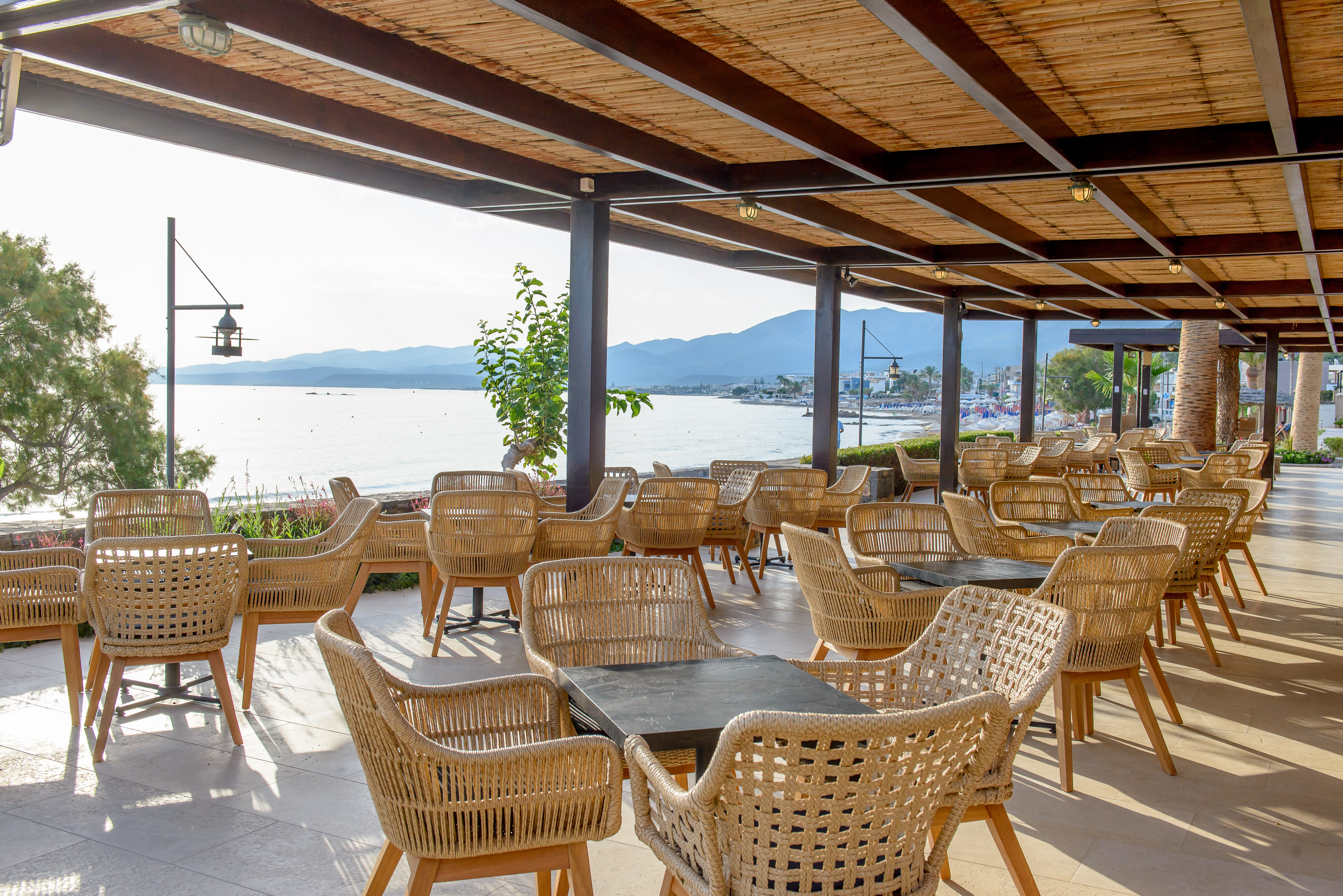 Beachfront restaurant patio with wicker chairs, sea view, and bamboo roof.