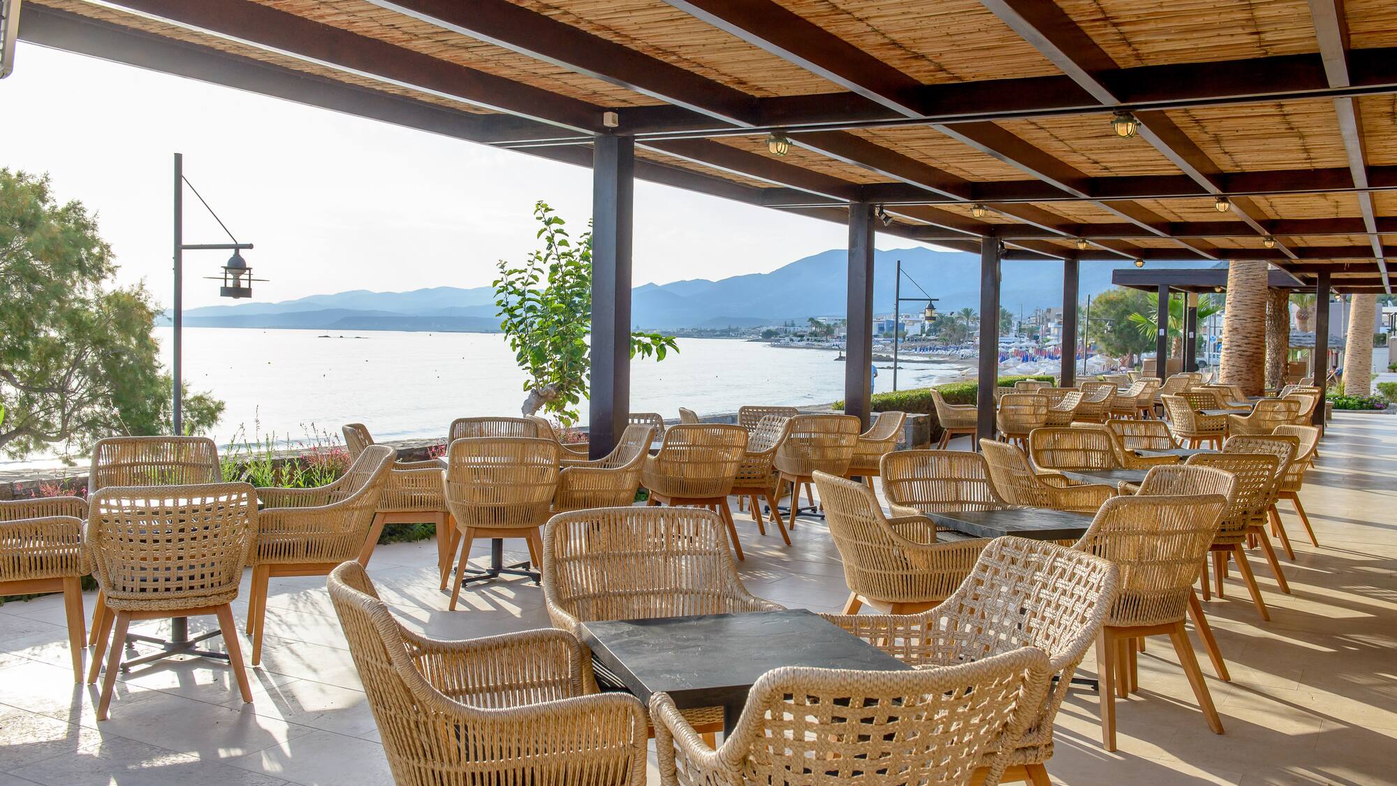 Beachfront restaurant patio with wicker chairs, sea view, and bamboo roof.