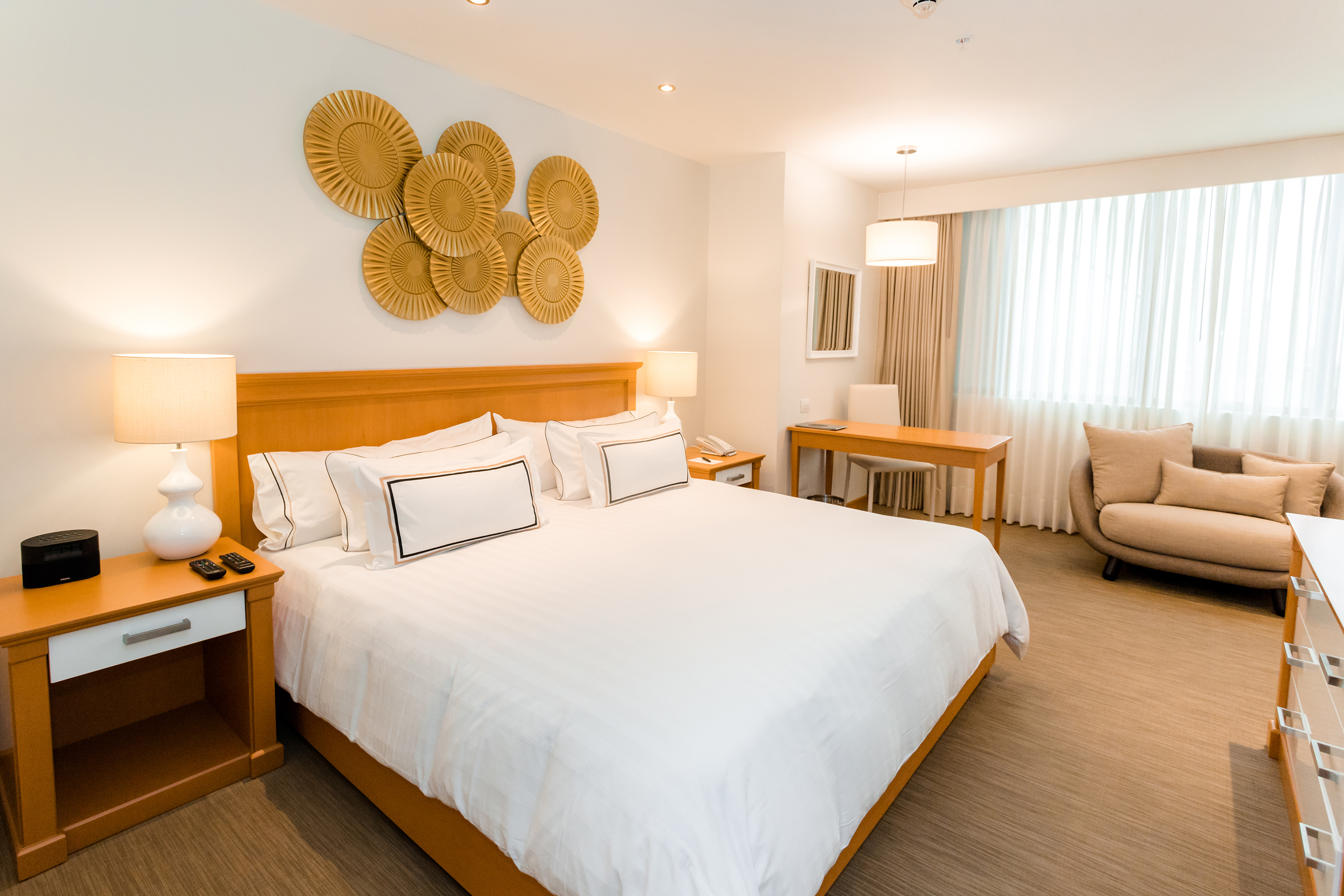 Hotel room with king bed, wooden headboard, circular gold wall decor, and desk.