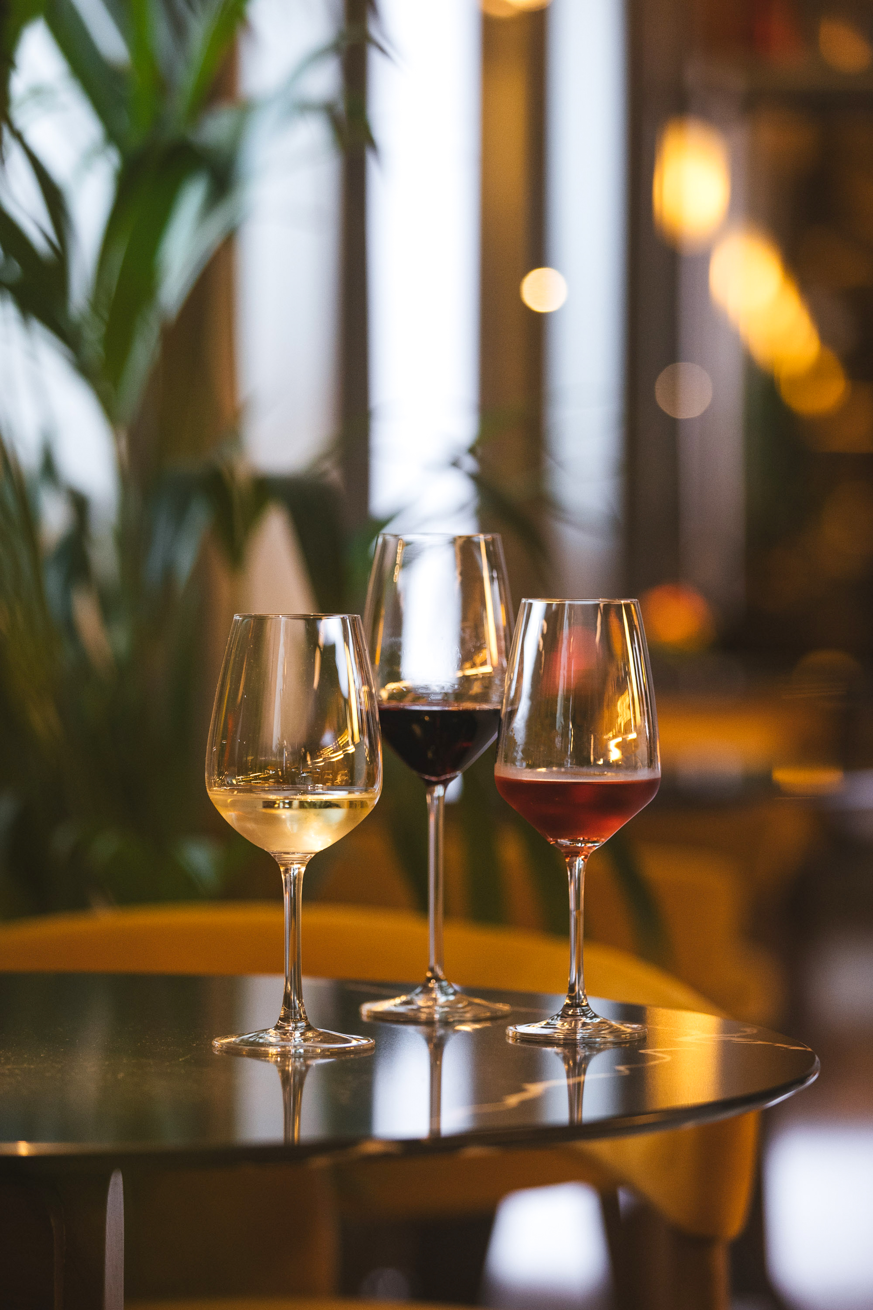 Three wine glasses with white, red, and rosé wine on a dark table in a restaurant.