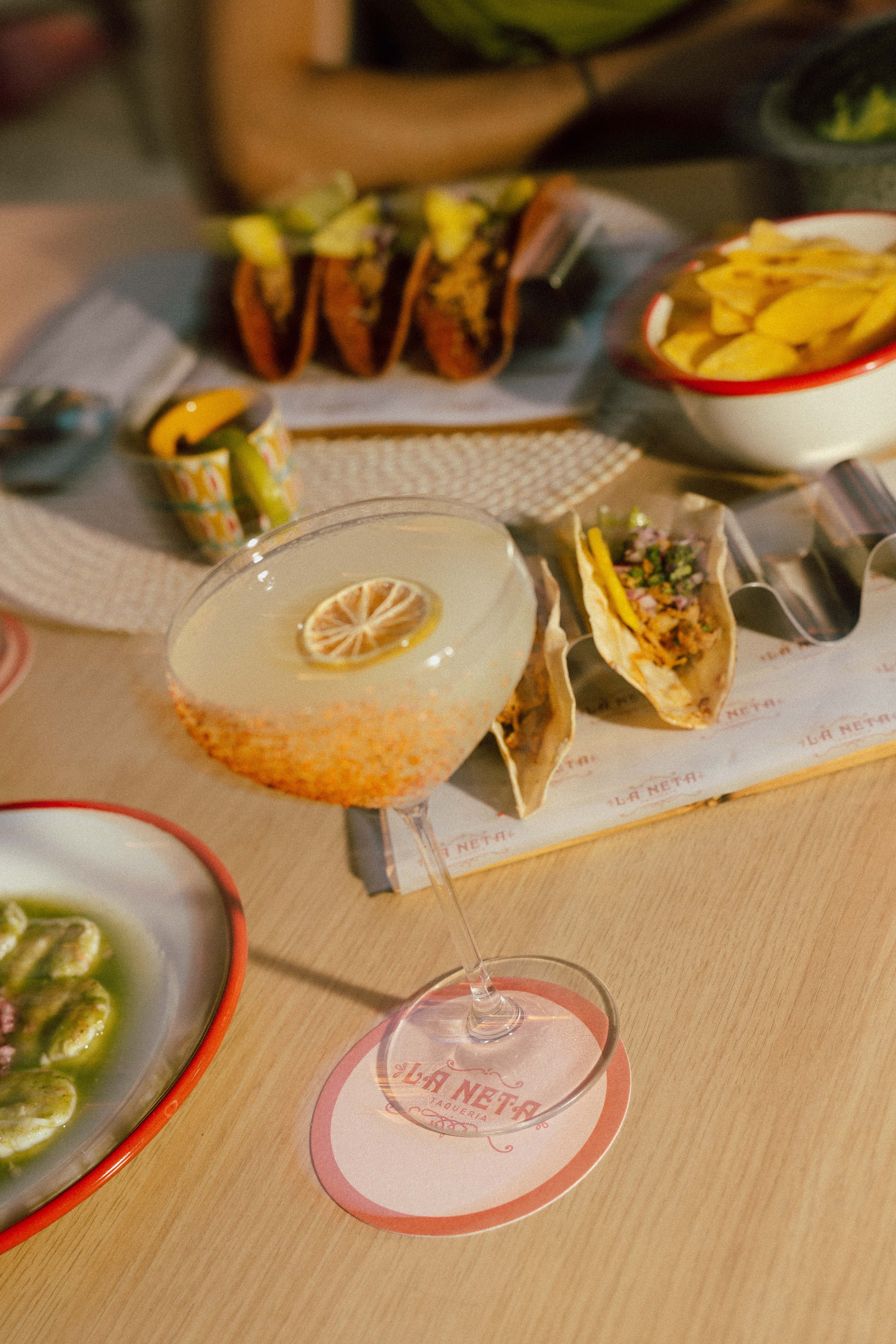 Tacos, citrus cocktail, and chips on a table at La Neta Taqueria.