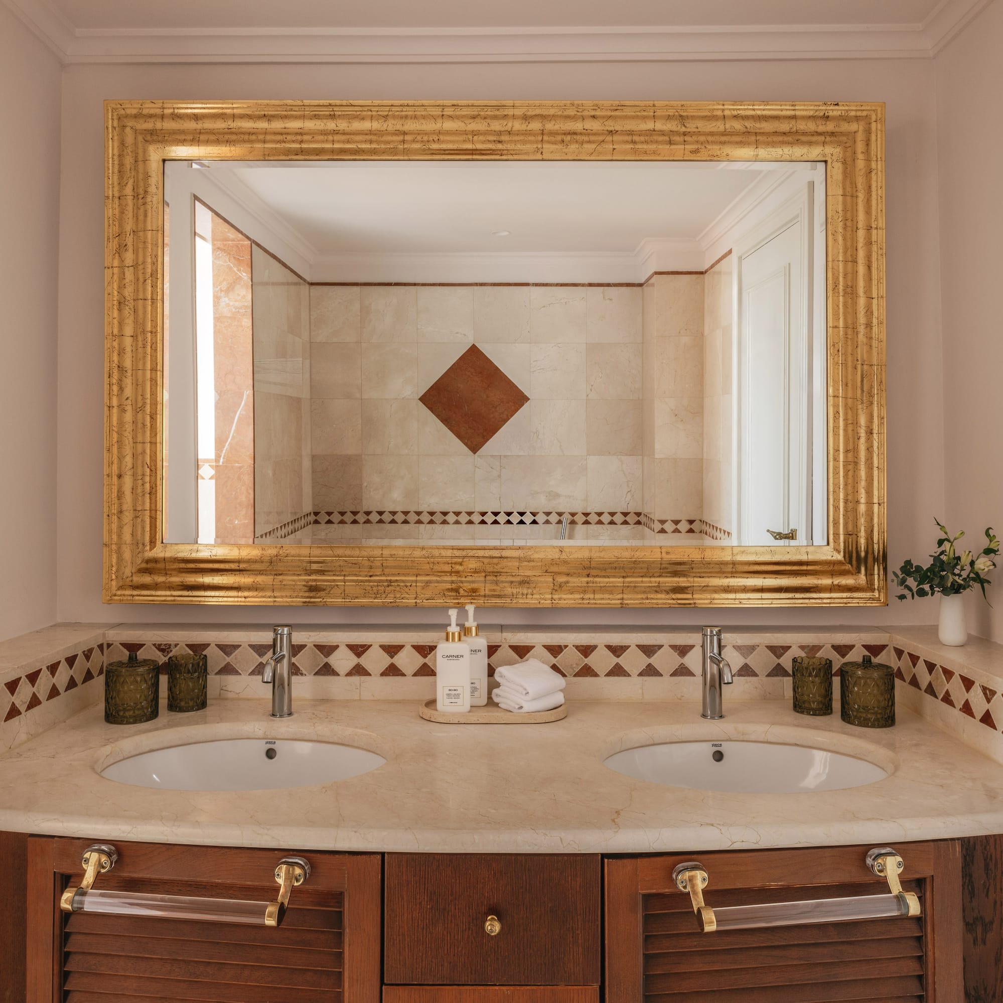 Luxury bathroom vanity with double sinks, marble top, and ornate gold mirror.