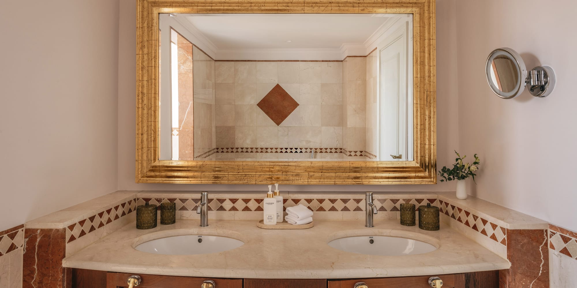 Luxury bathroom vanity with double sinks, marble top, and ornate gold mirror.