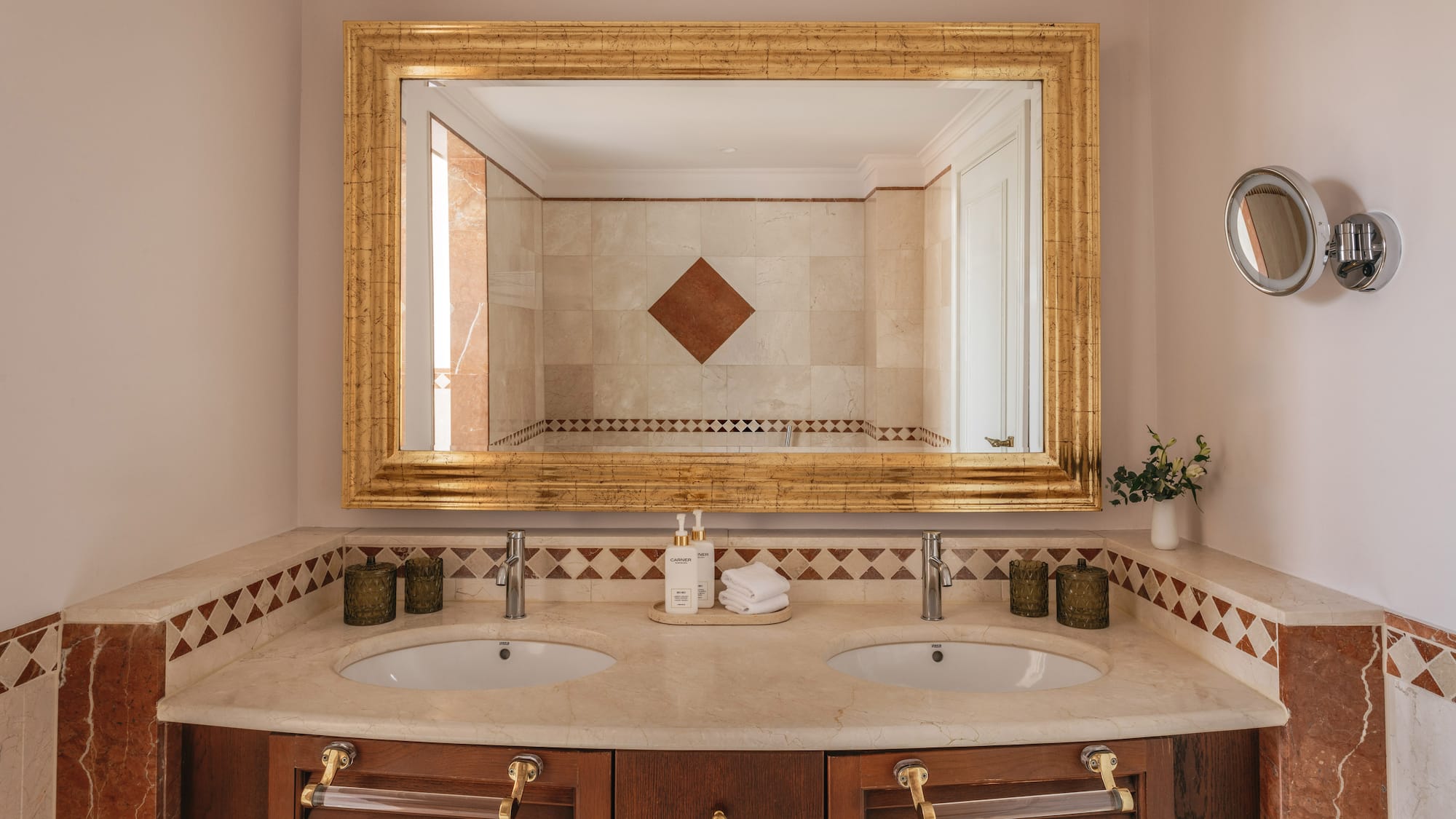 Luxury bathroom vanity with double sinks, marble top, and ornate gold mirror.