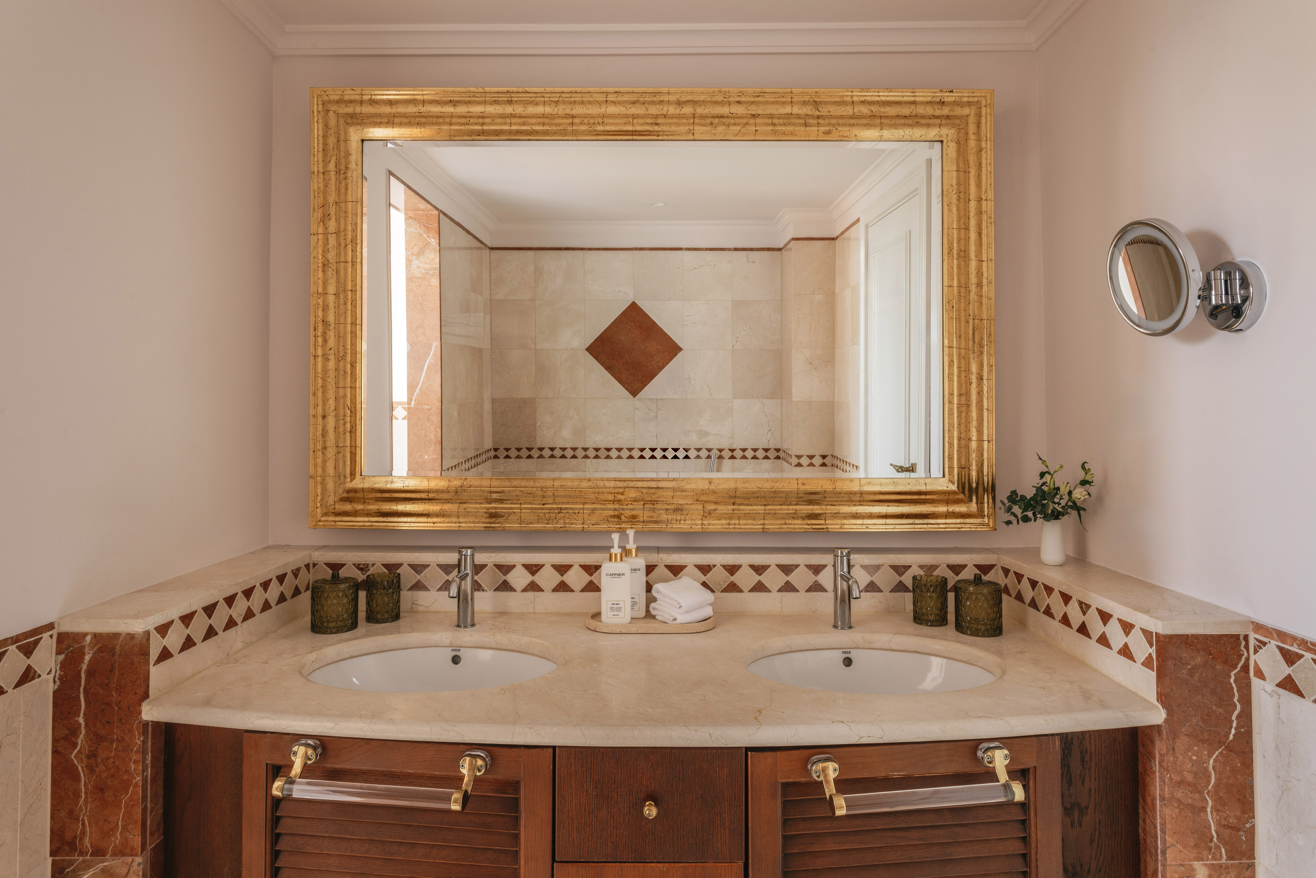 Luxury bathroom vanity with double sinks, marble top, and ornate gold mirror.
