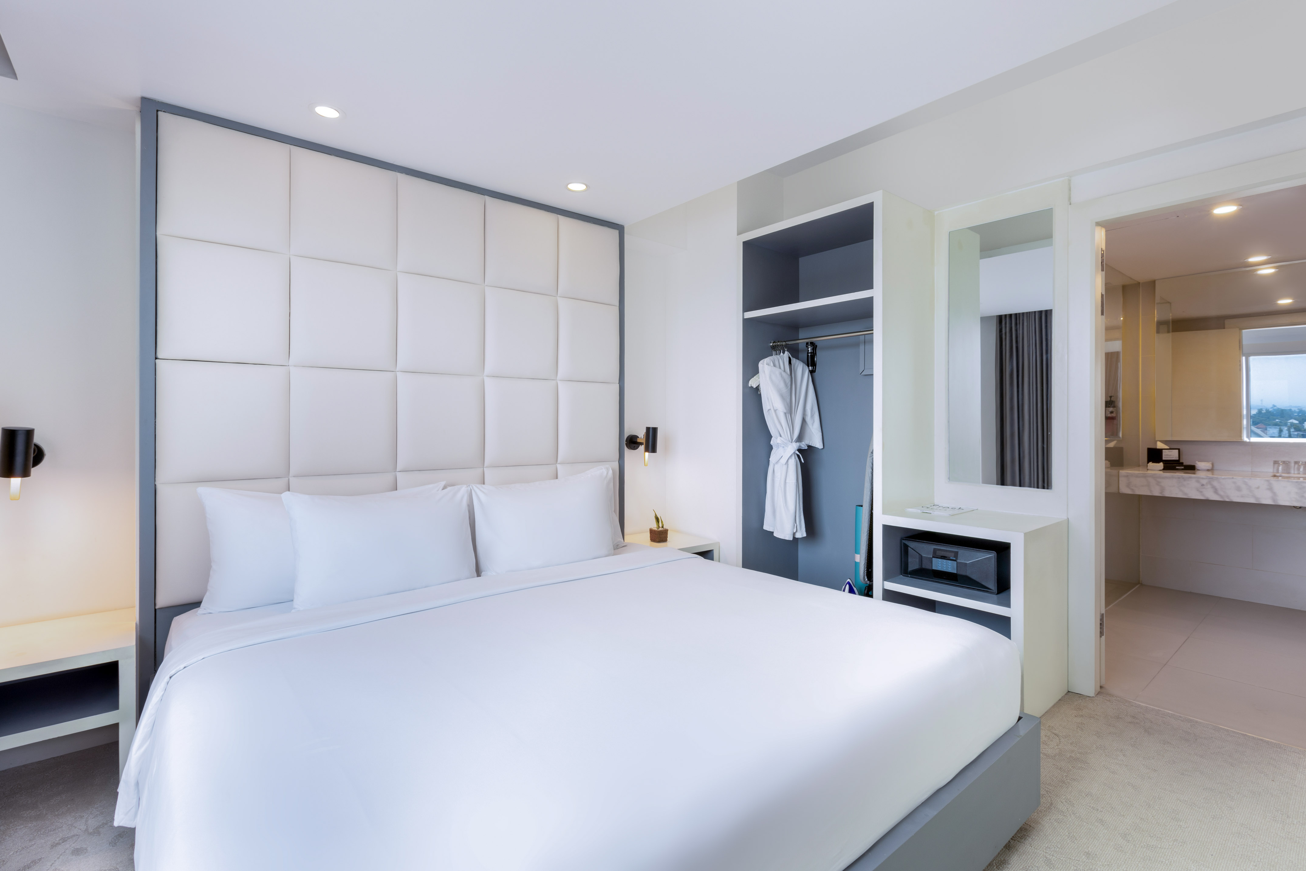 Modern hotel bedroom with queen bed, white bedding, built-in closet, and safe.