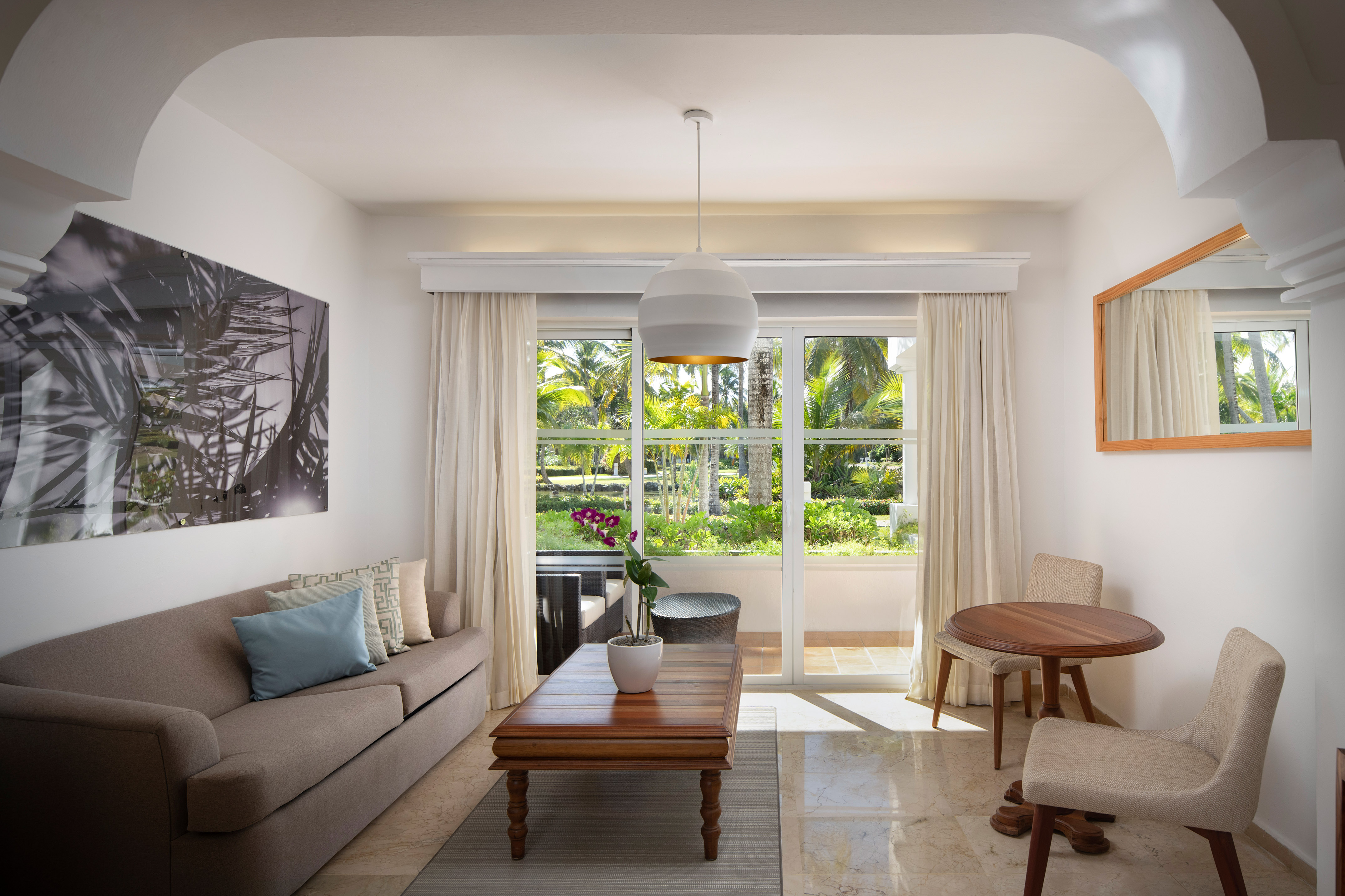 Modern hotel suite living room with tropical garden view, sofa, and dining area.