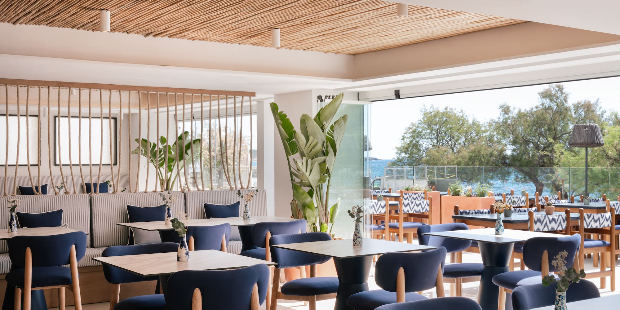 Modern restaurant interior with blue chairs, wood tables, and ocean view.