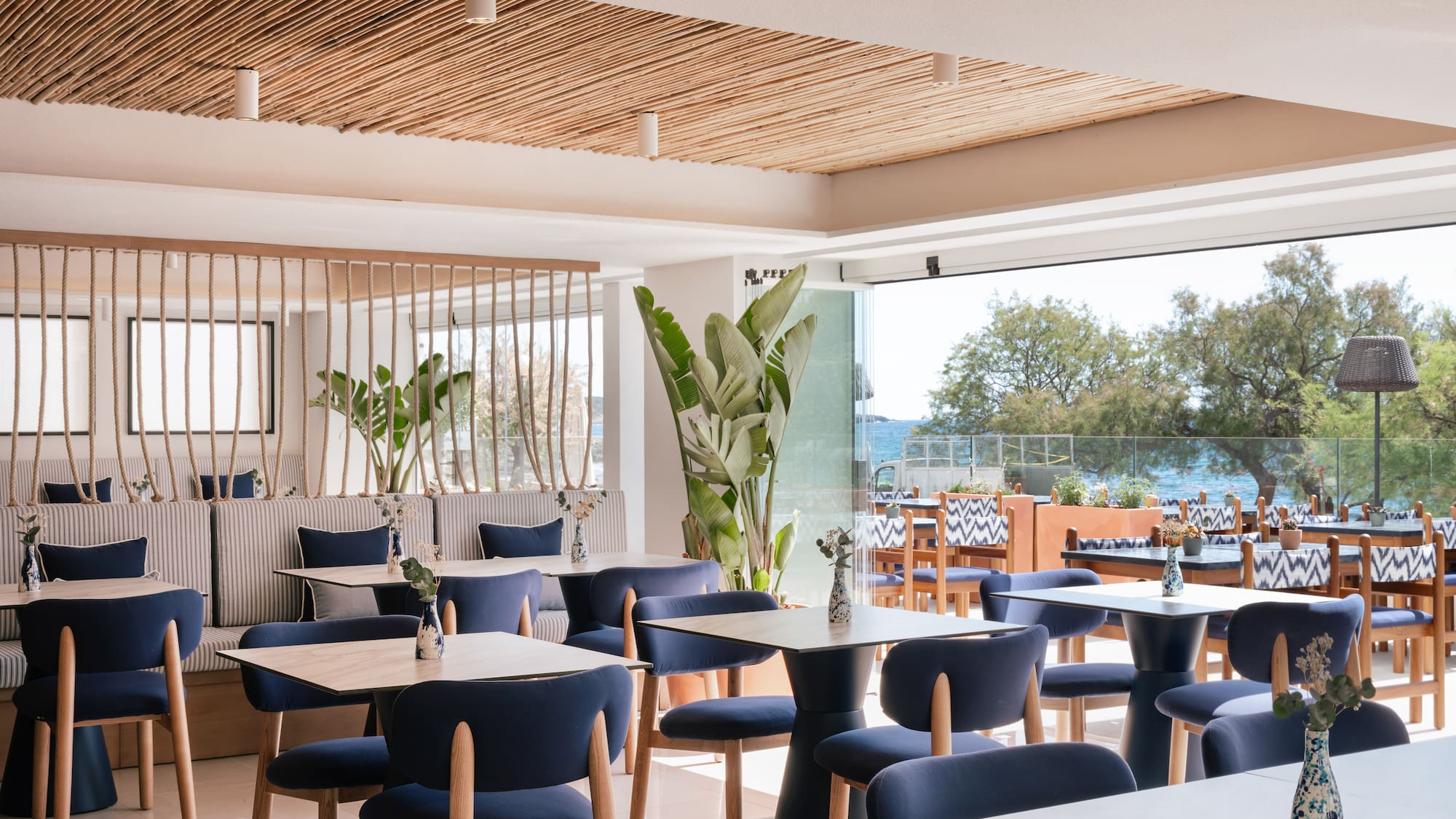 Modern restaurant interior with blue chairs, wood tables, and ocean view.