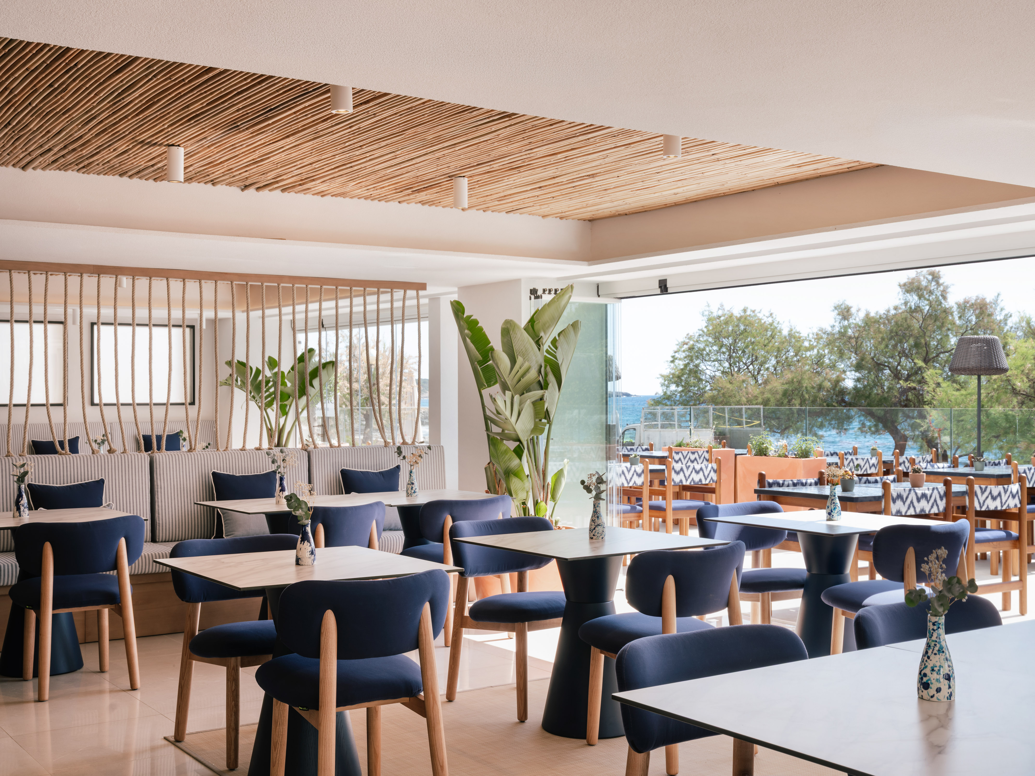 Modern restaurant interior with blue chairs, wood tables, and ocean view.
