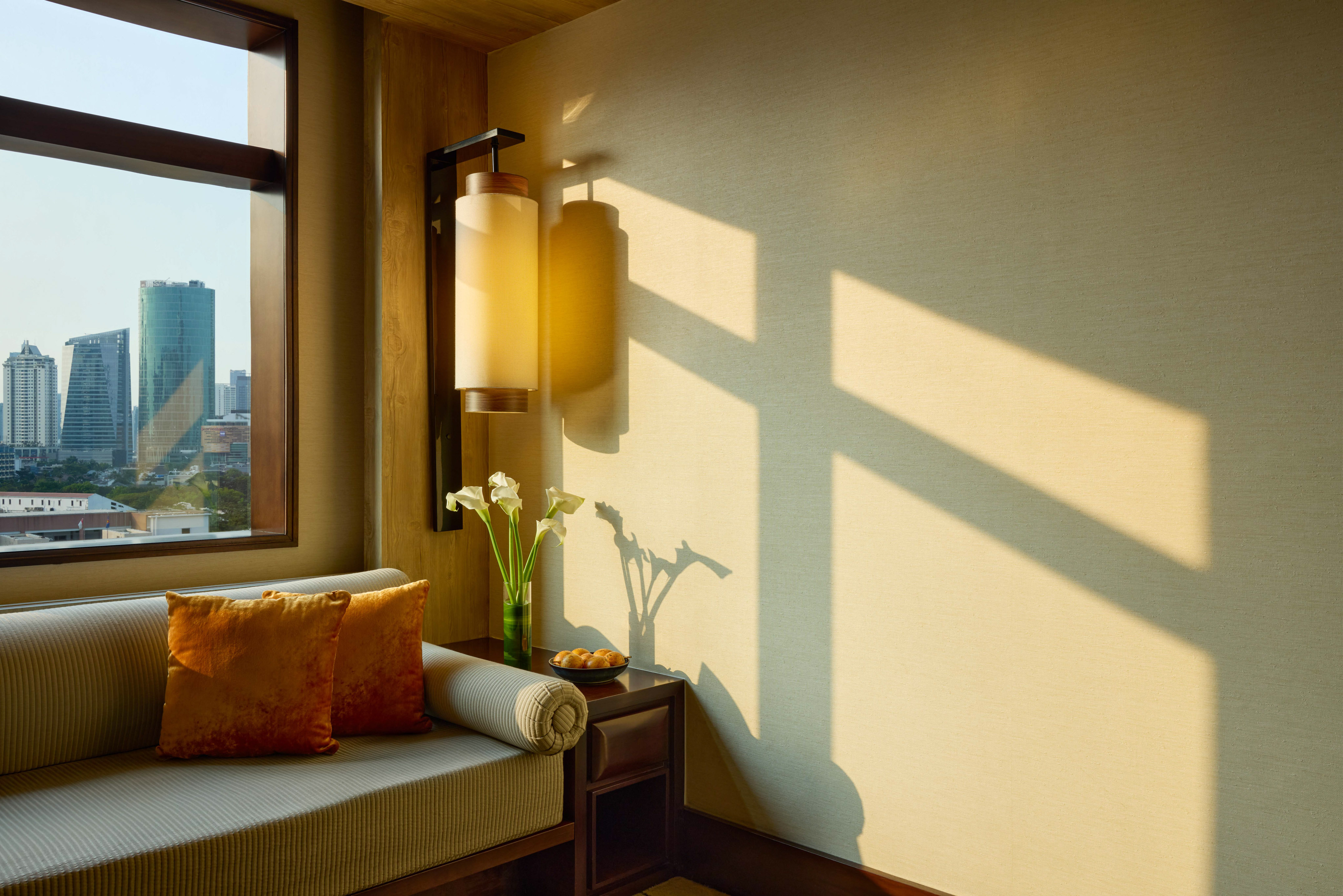 Sunlit modern hotel room with city skyline view and cozy sofa.