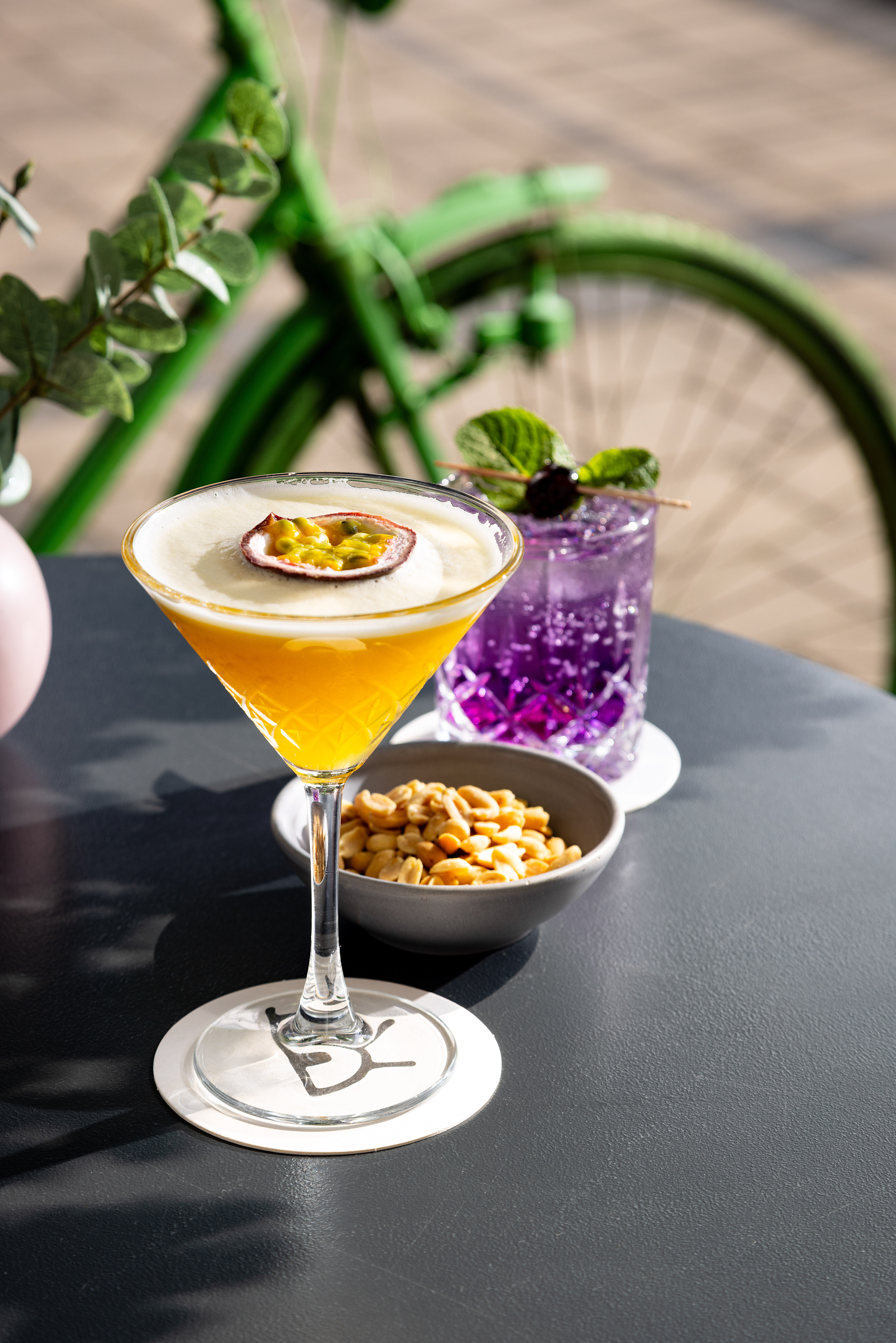 Passion fruit martini, purple cocktail, peanuts on outdoor table with green bike.