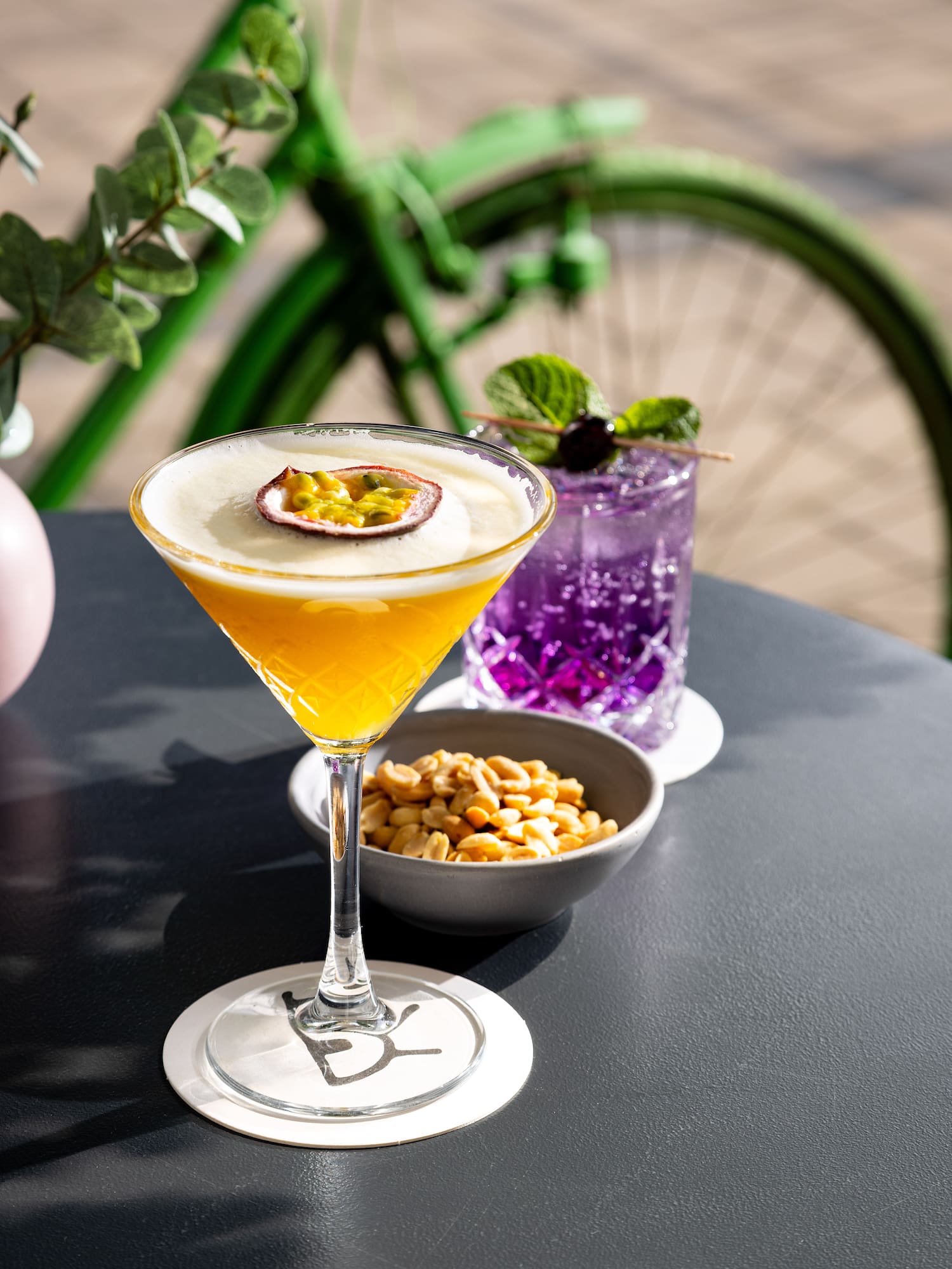Passion fruit martini, purple cocktail, peanuts on outdoor table with green bike.