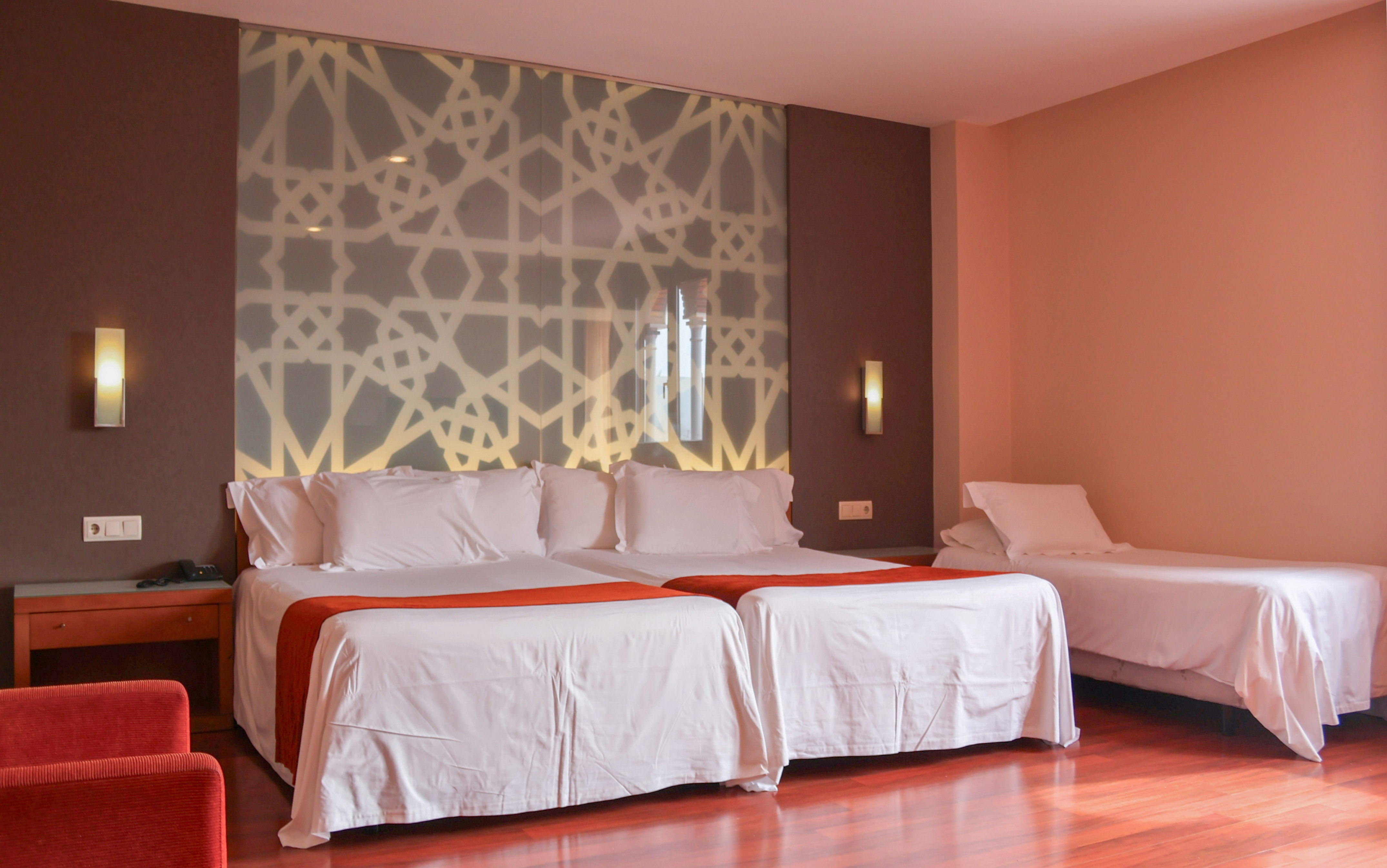 Modern triple hotel room with geometric pattern headboard.