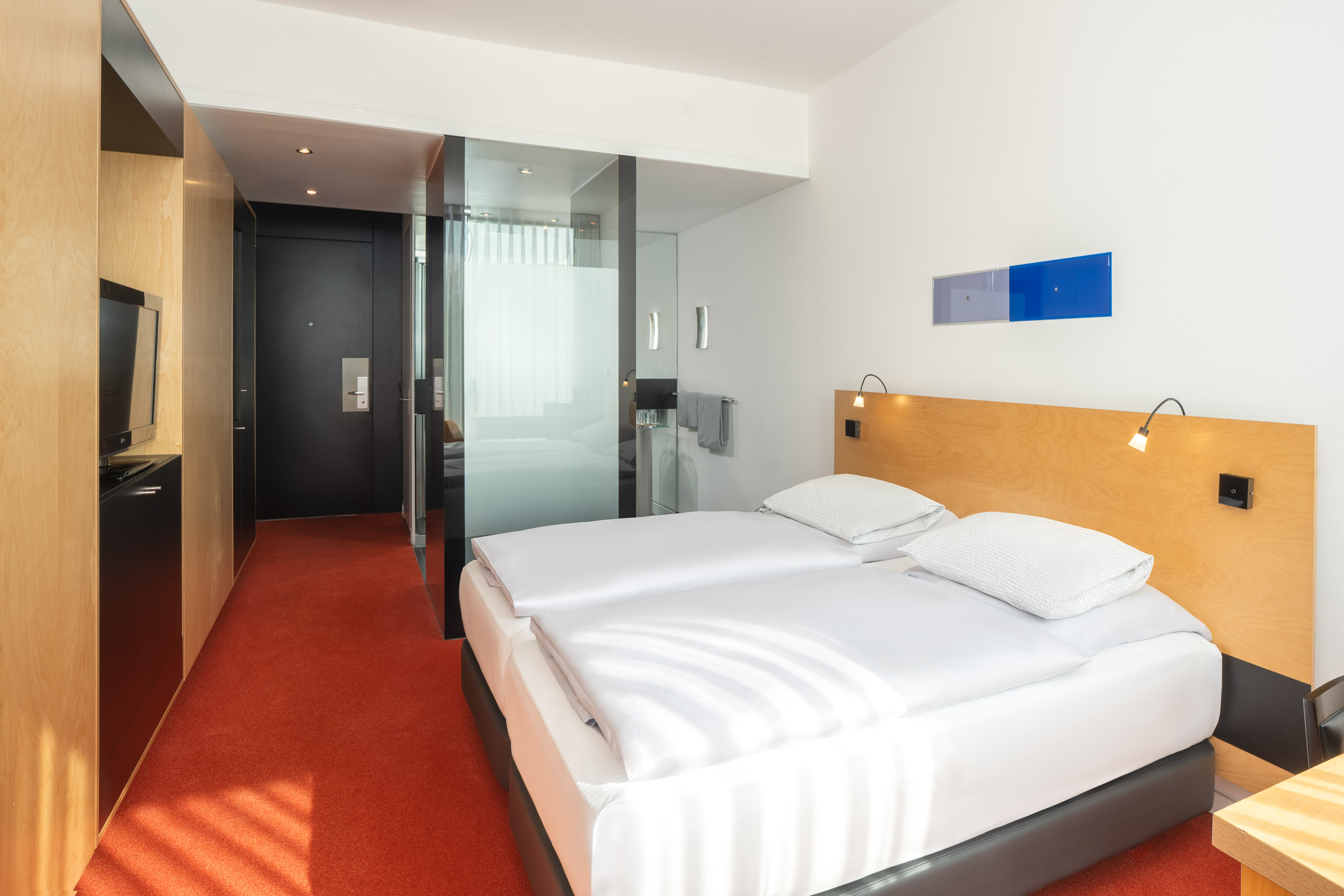 Modern hotel room with twin beds, wooden headboard, red carpet, and sleek design. - The INNSiDE Room - INNSiDE Düsseldorf Seestern, Düsseldorf