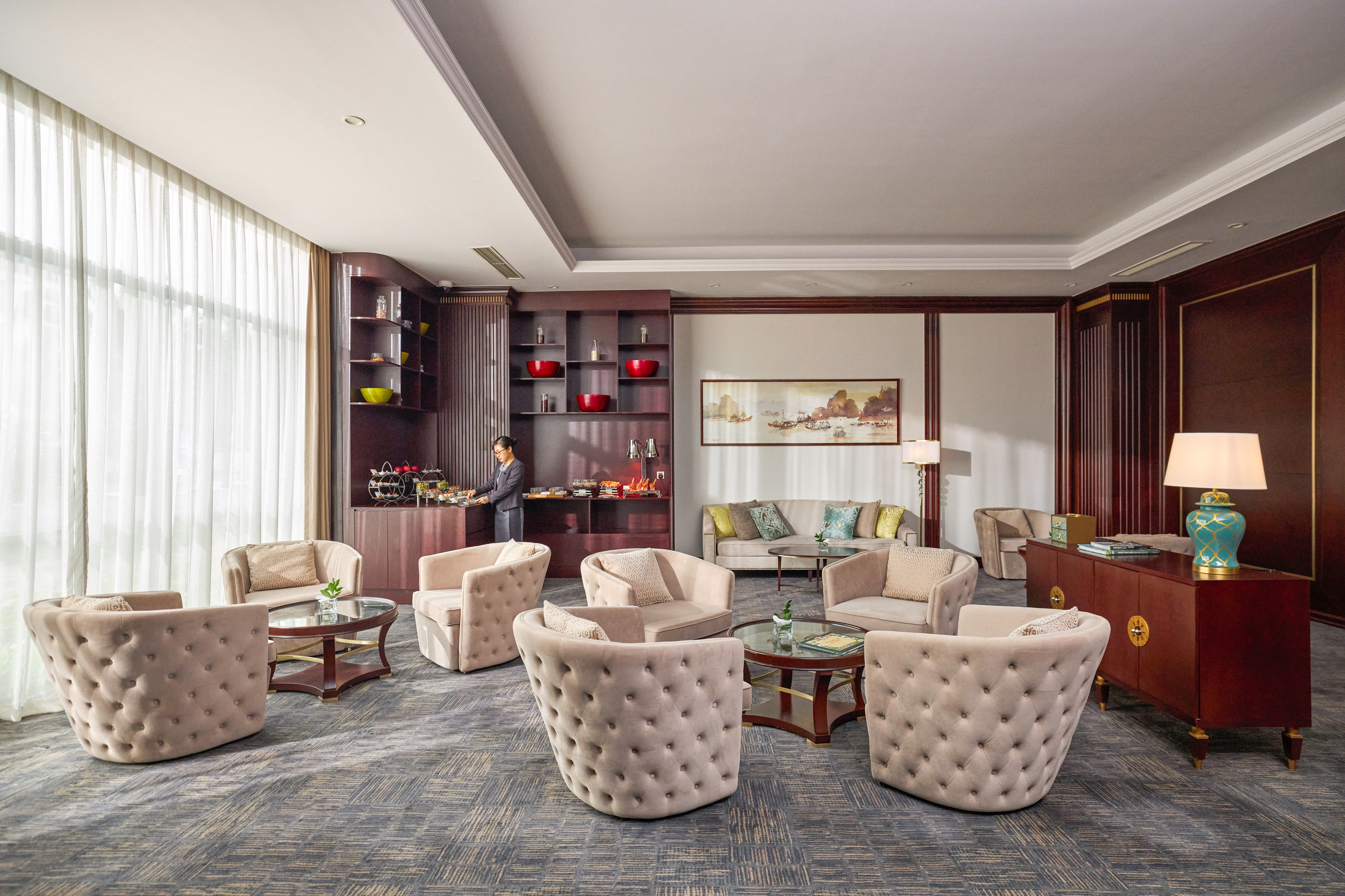 Elegant hotel lounge with plush seating, buffet, and a staff member.