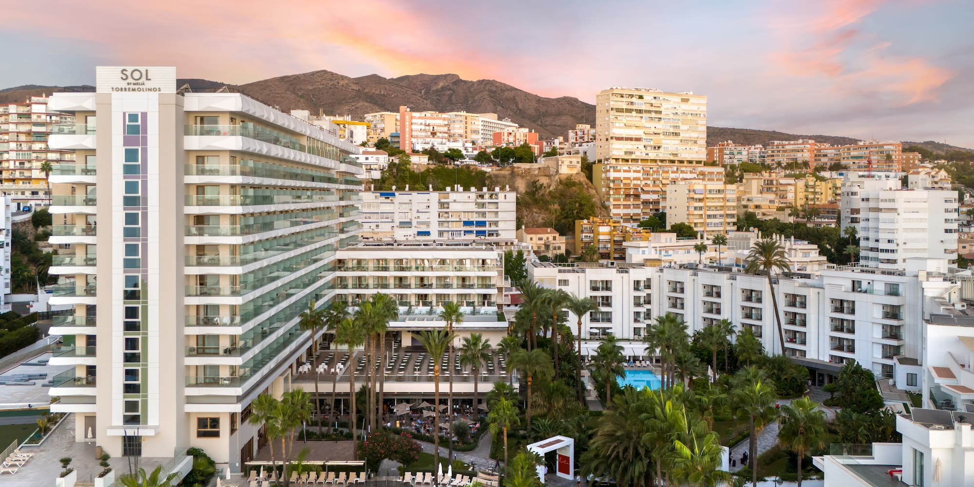 a group of buildings with palm trees and mountains in the background