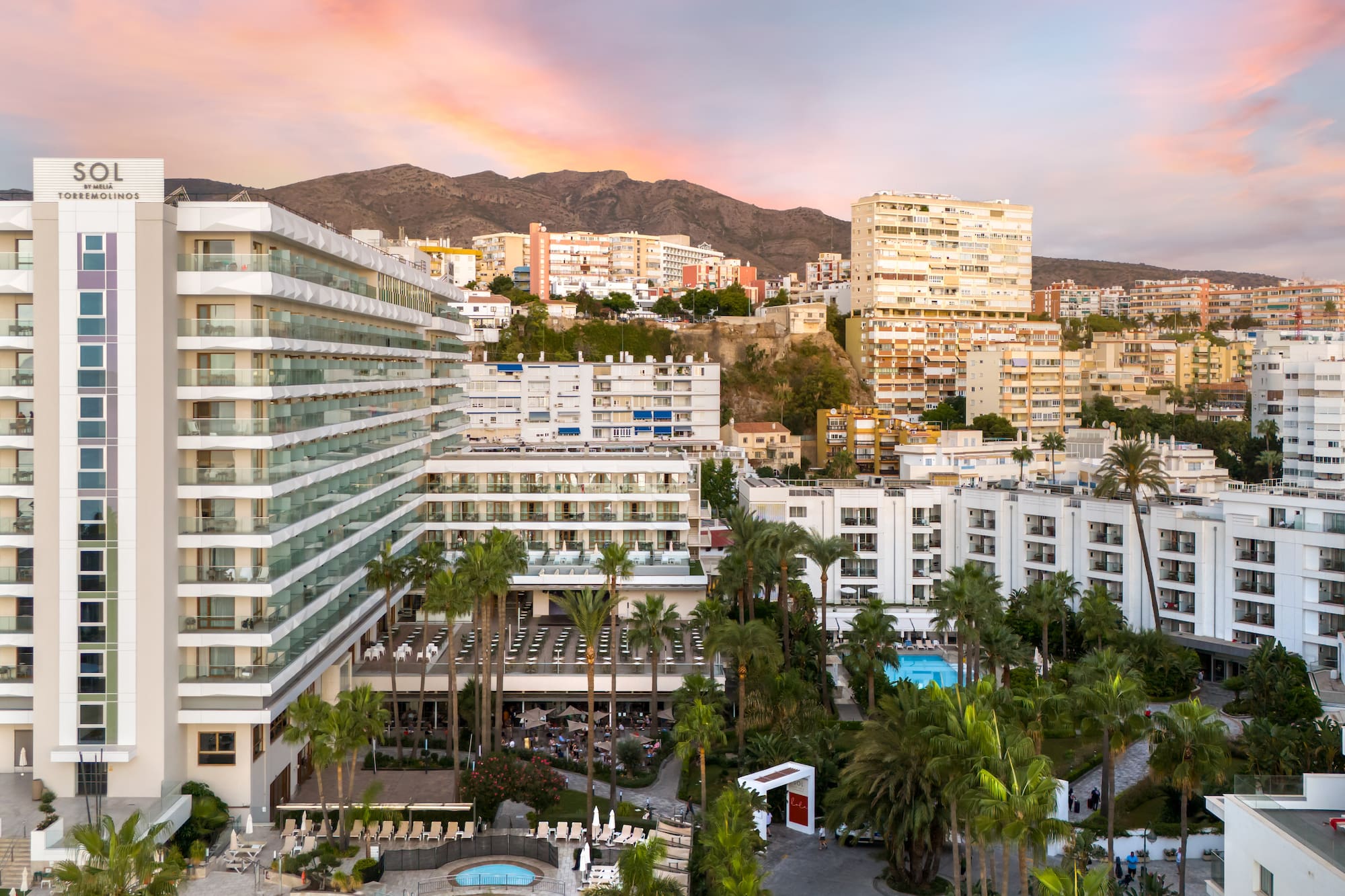 a group of buildings with palm trees and mountains in the background