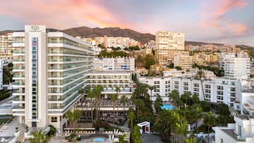 a group of buildings with palm trees and mountains in the background