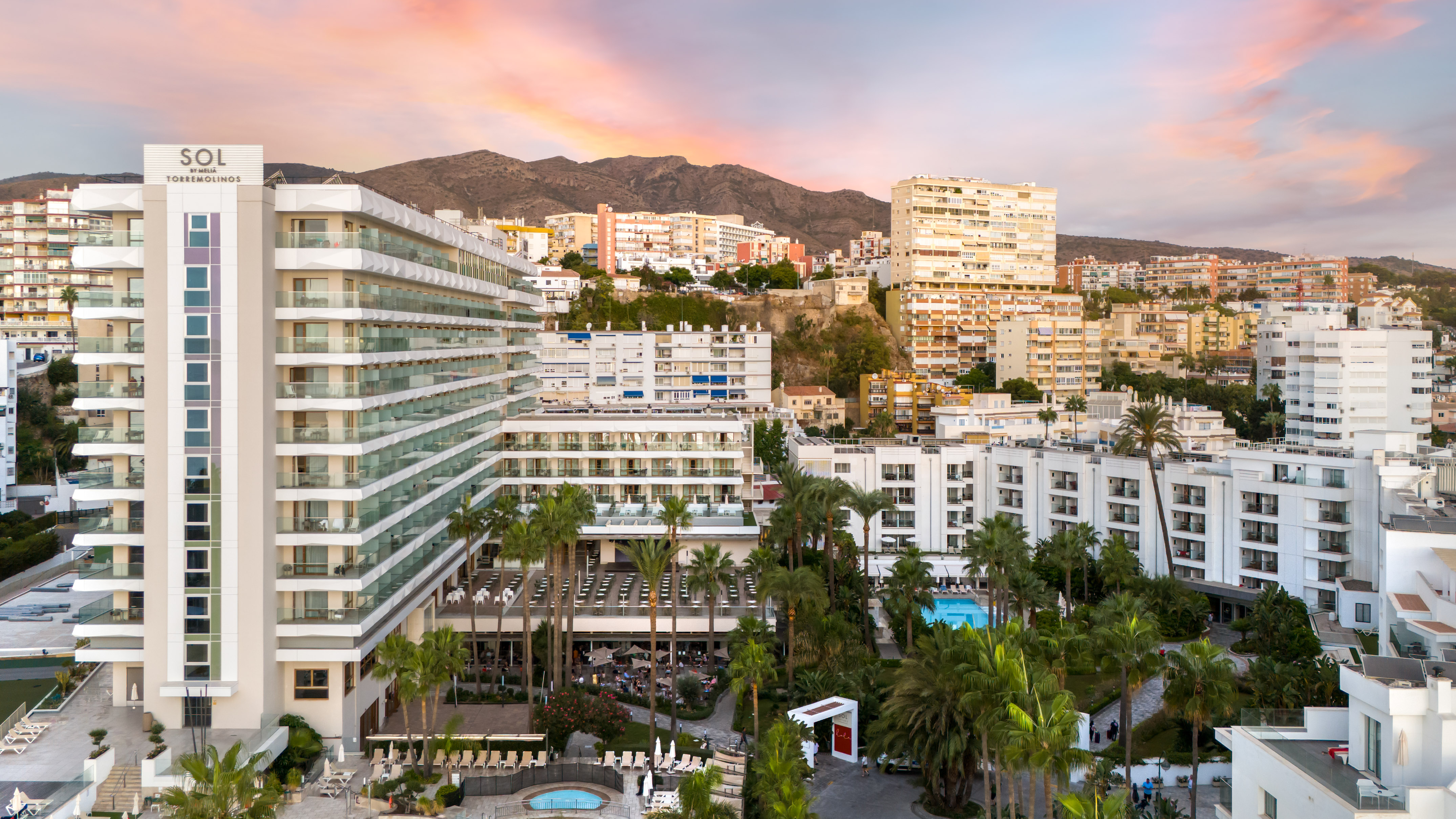 Sol Torremolinos hotel resort, pools, palm trees, and mountains at sunset.