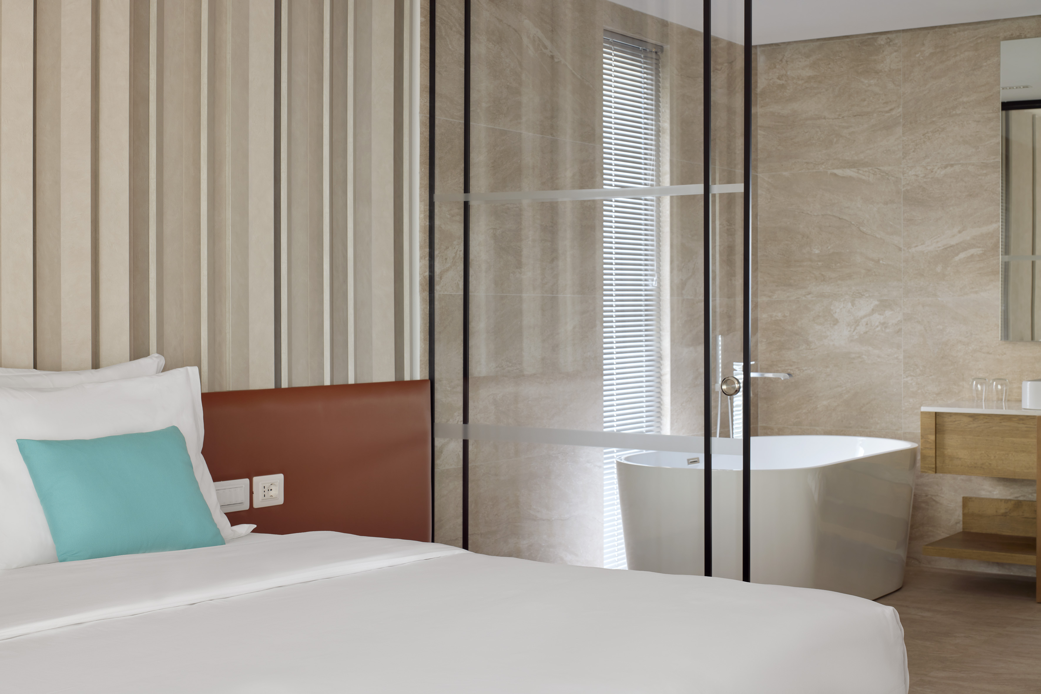 Modern hotel bedroom suite with glass-enclosed bathroom and freestanding tub.