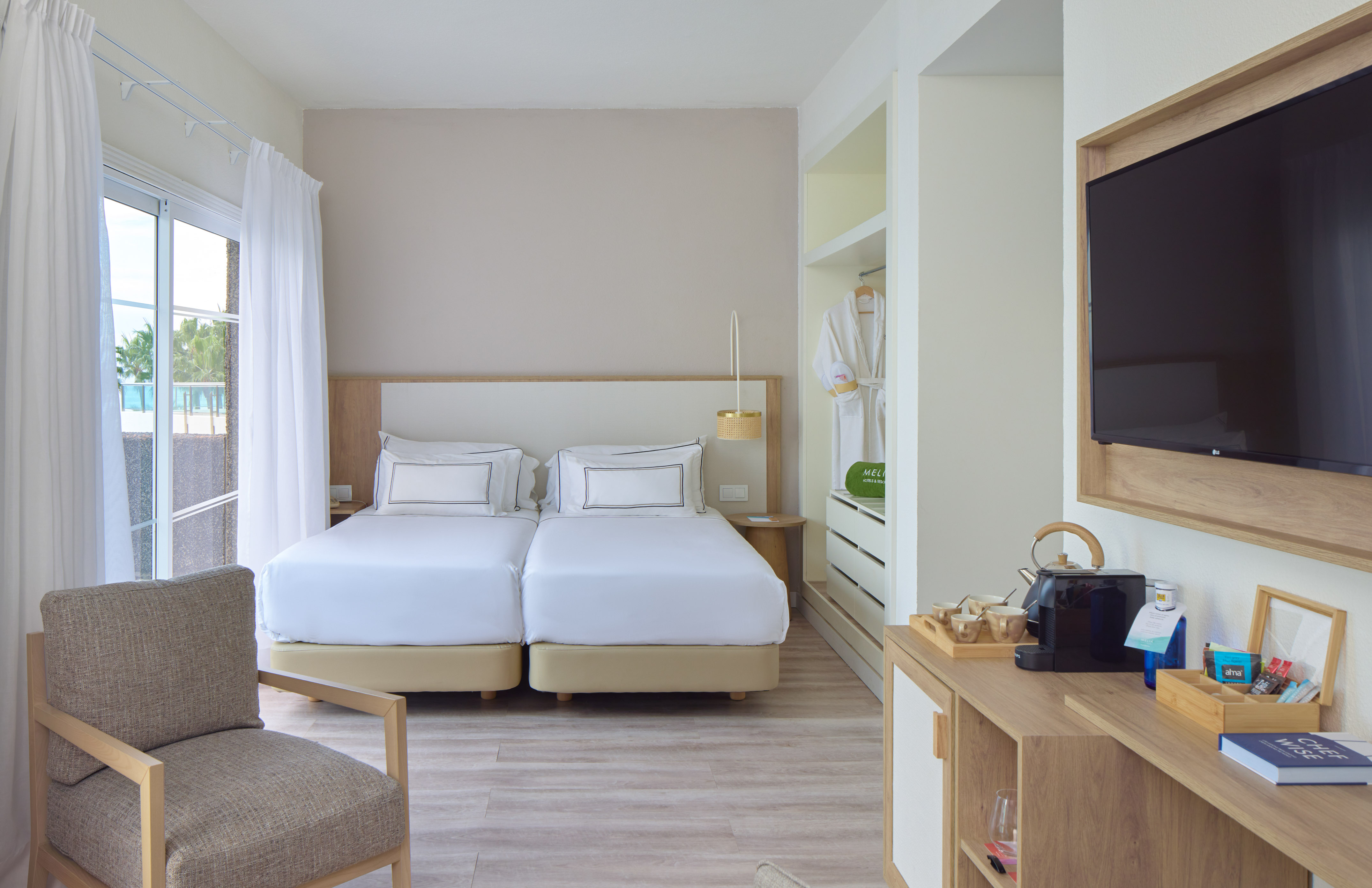 Stylish hotel room with twin beds, balcony access, TV, and minibar.
