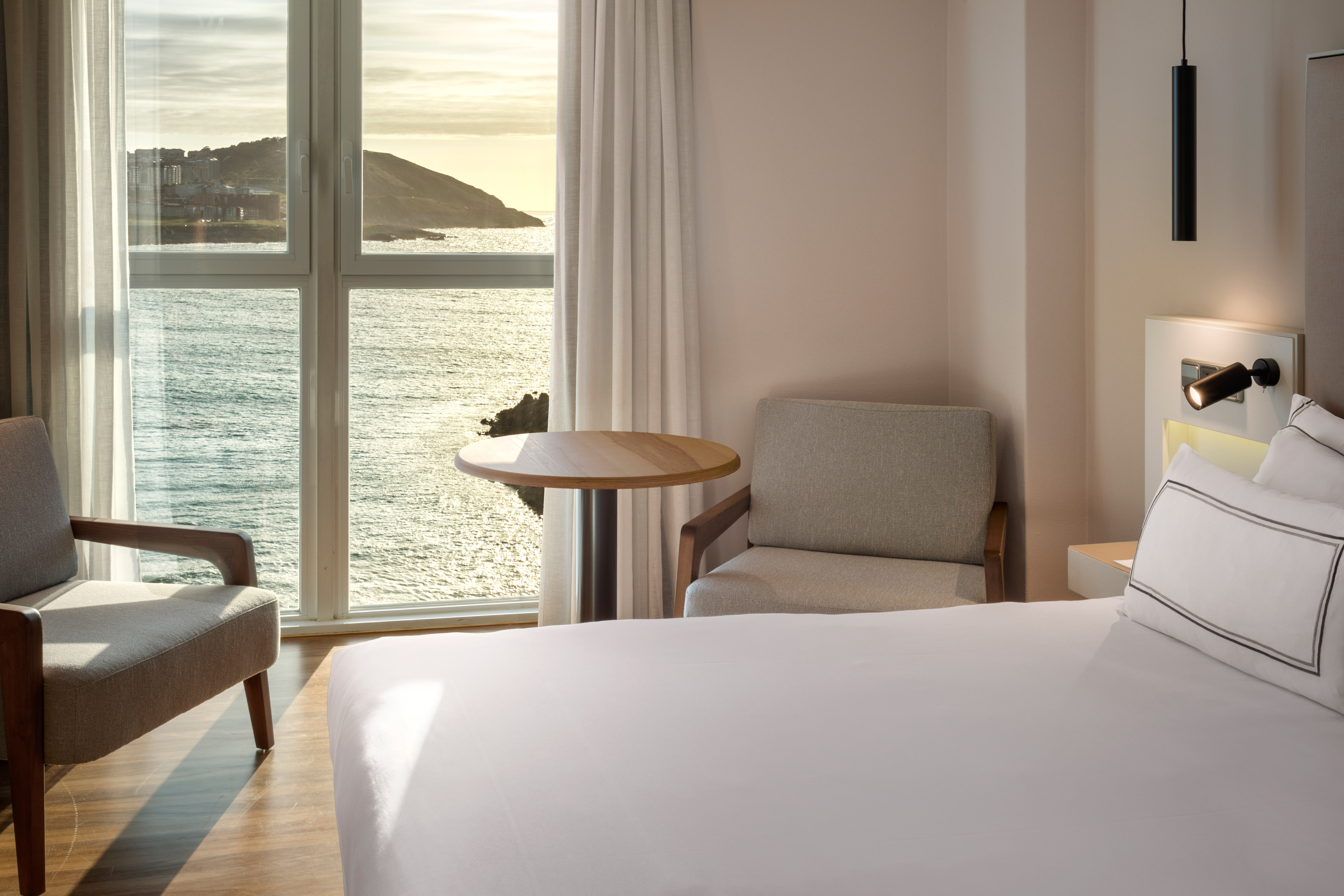 Bright hotel room with stunning sea view, bed, and window-side seating.