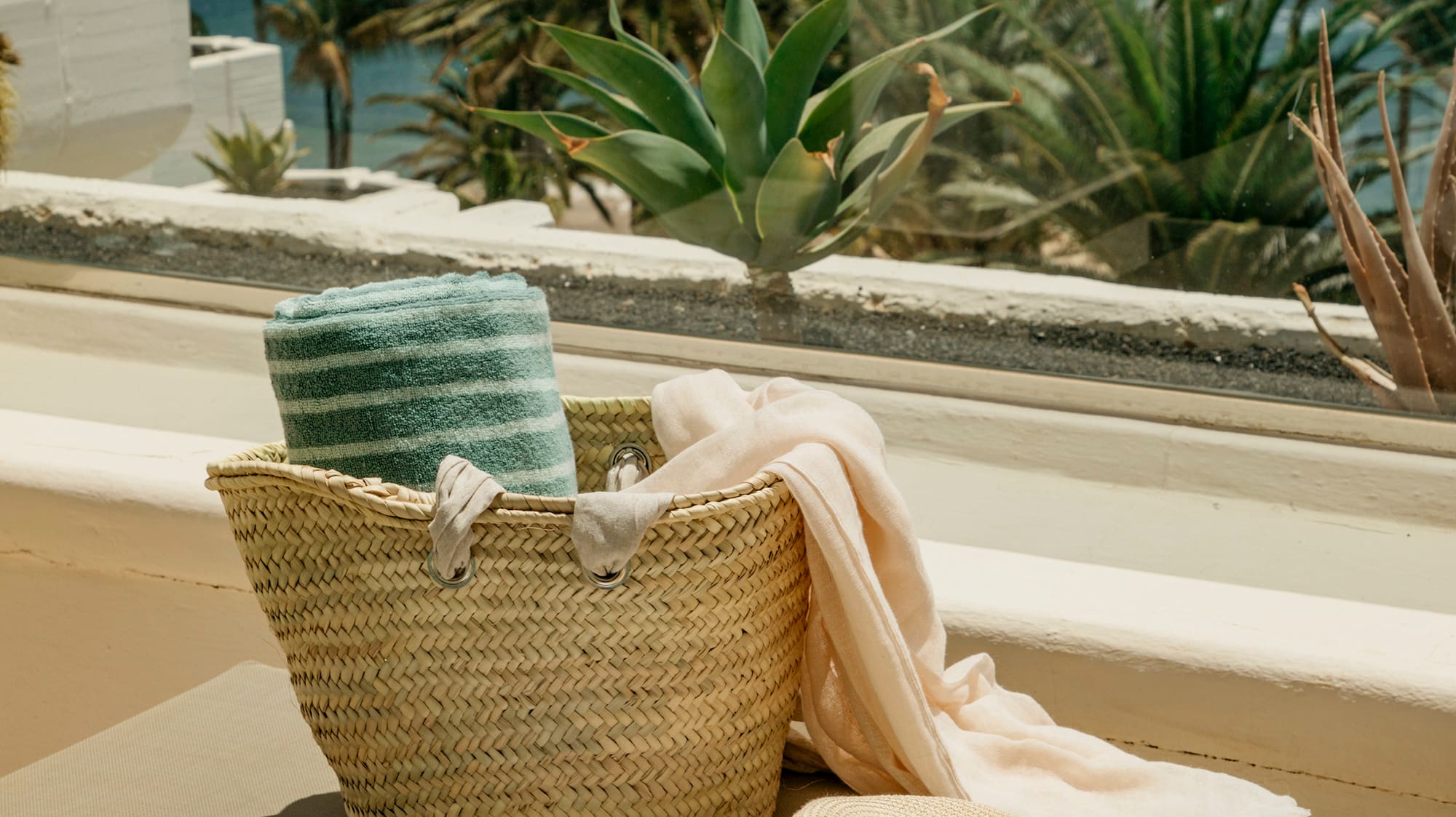 a hat and a basket on a bench outside by a window