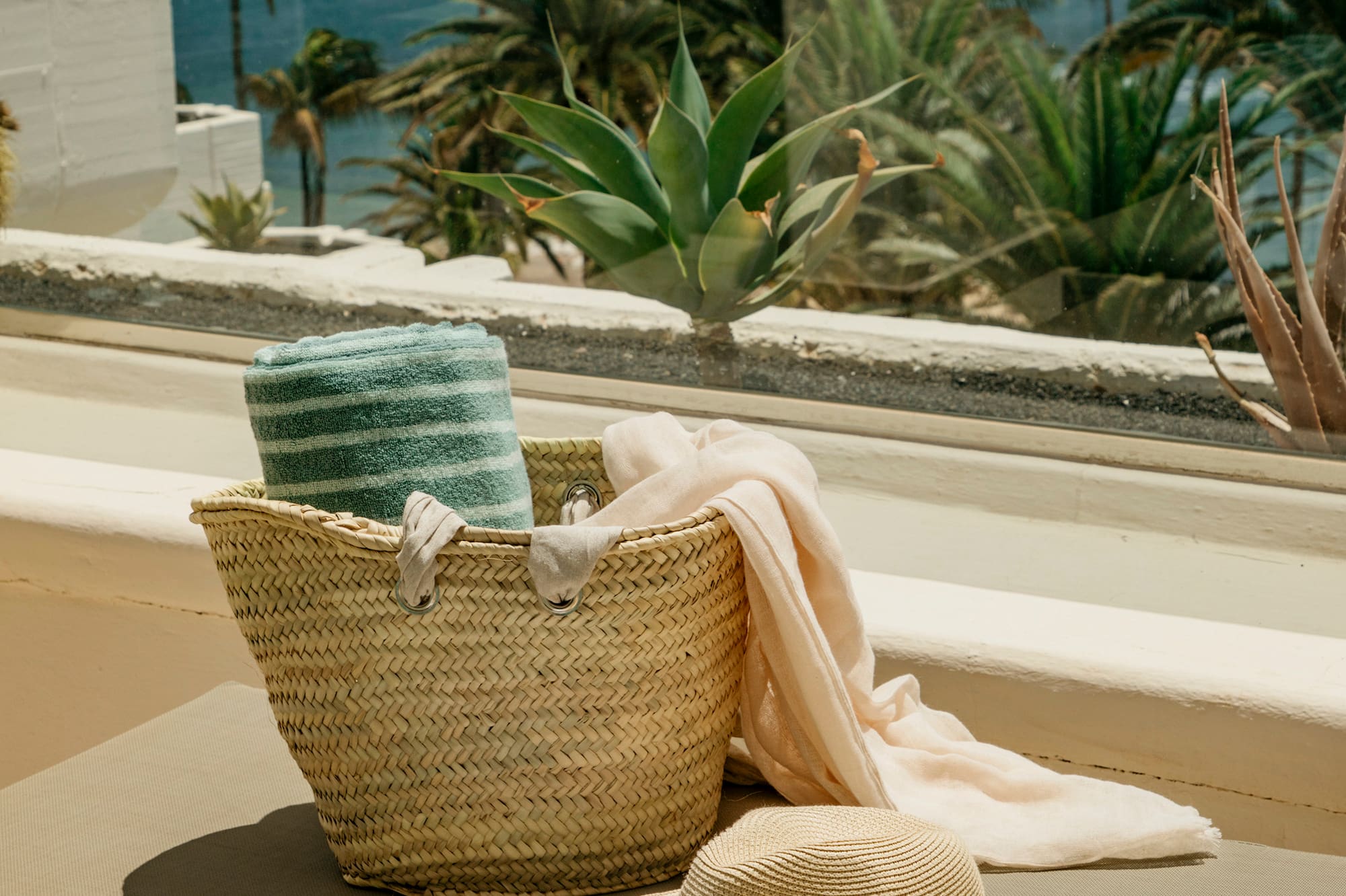 a hat and a basket on a bench outside by a window