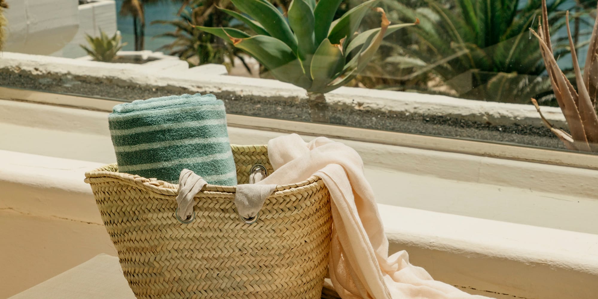 a hat and a basket on a bench outside by a window
