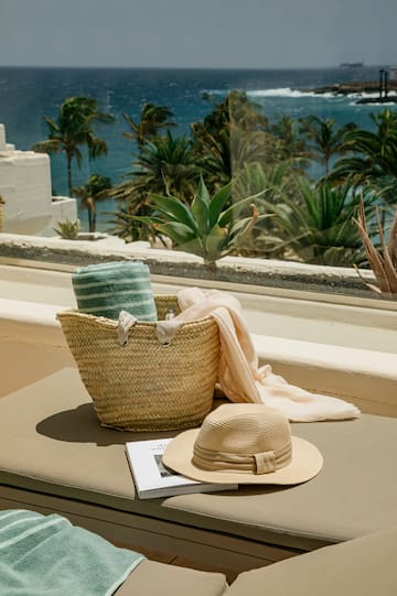 a hat and a basket on a bench outside by a window