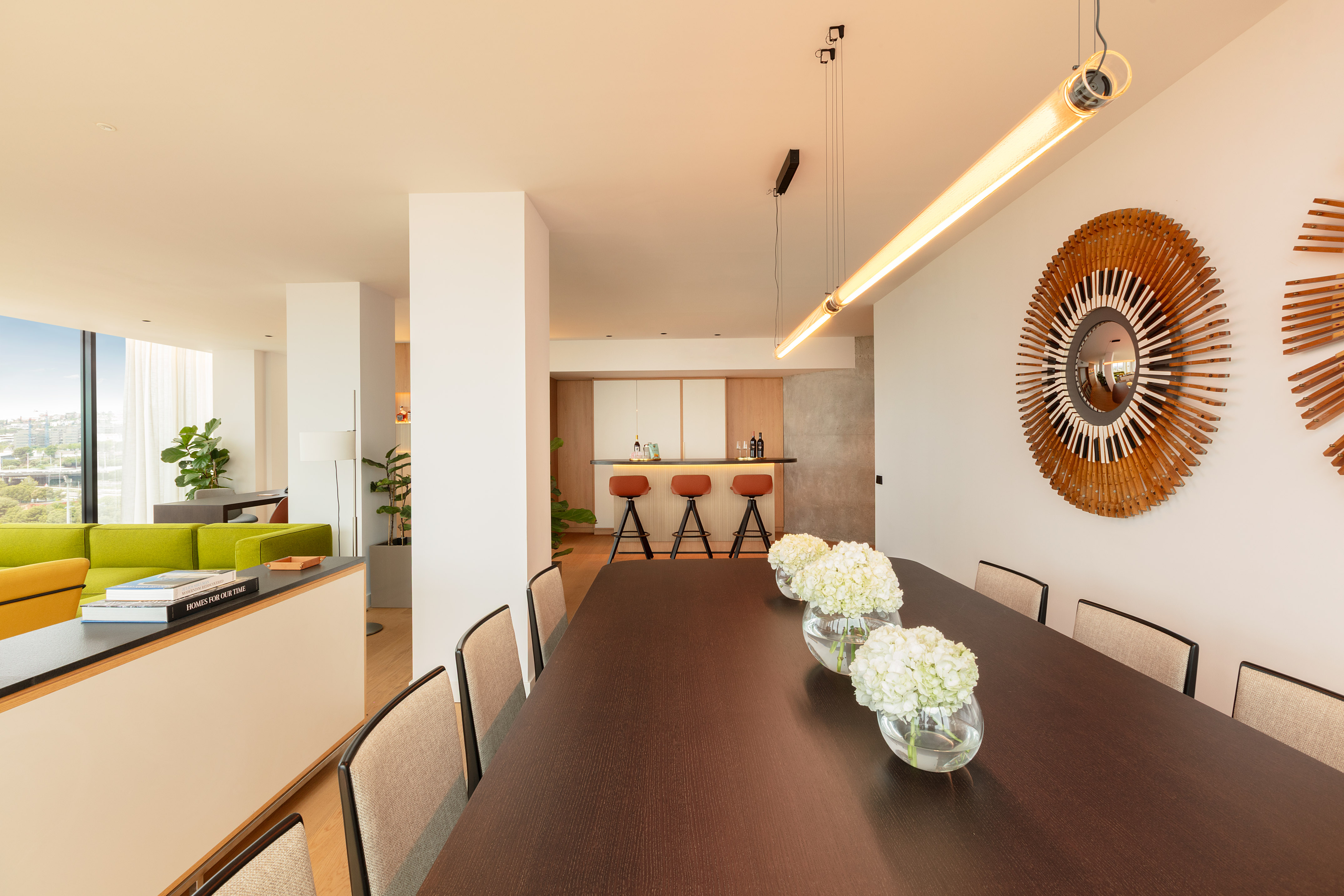 Contemporary dining room with dark table, hydrangeas, bar, and green sofa living area.