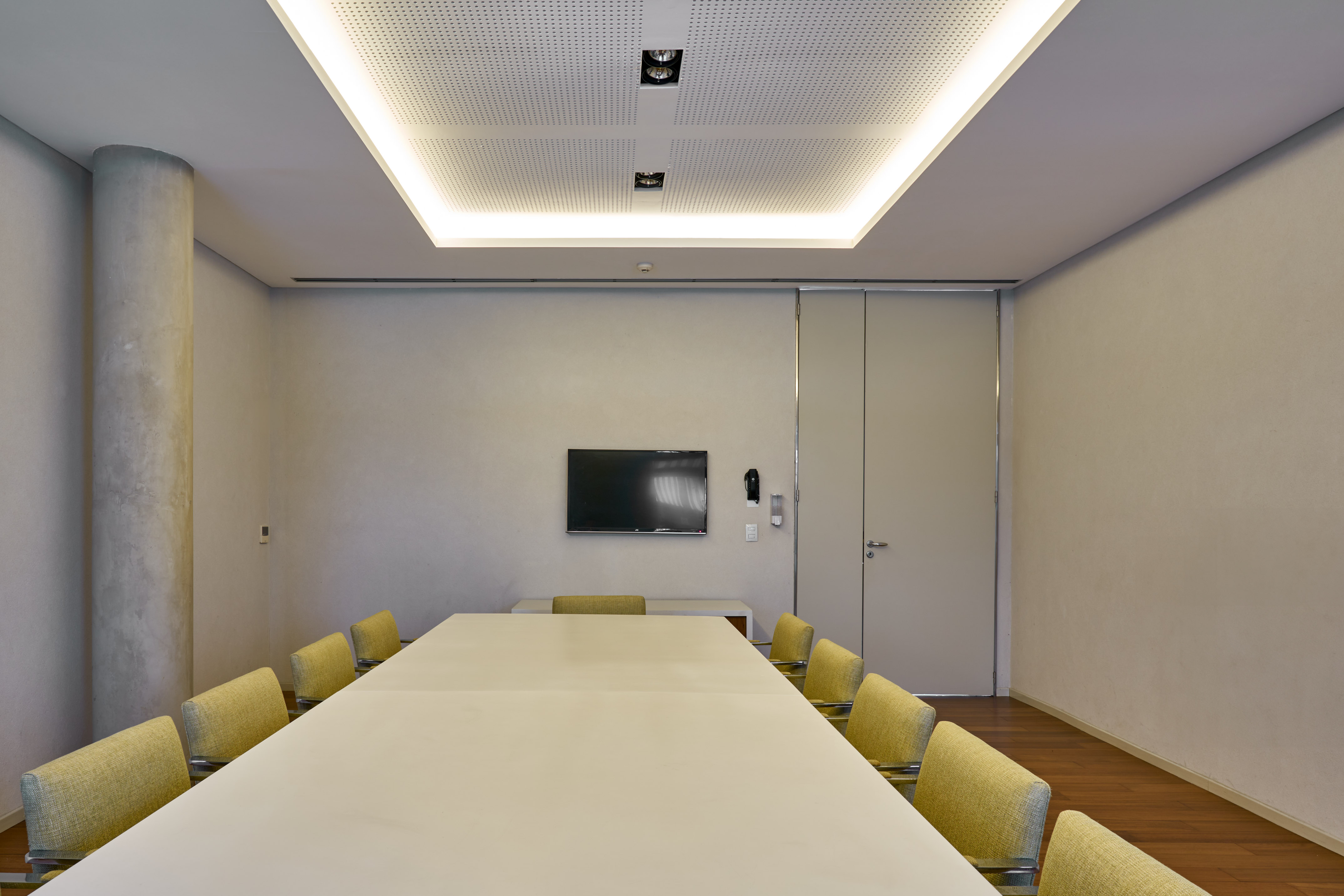 Modern conference room with long table, yellow chairs, TV, and recessed lighting.