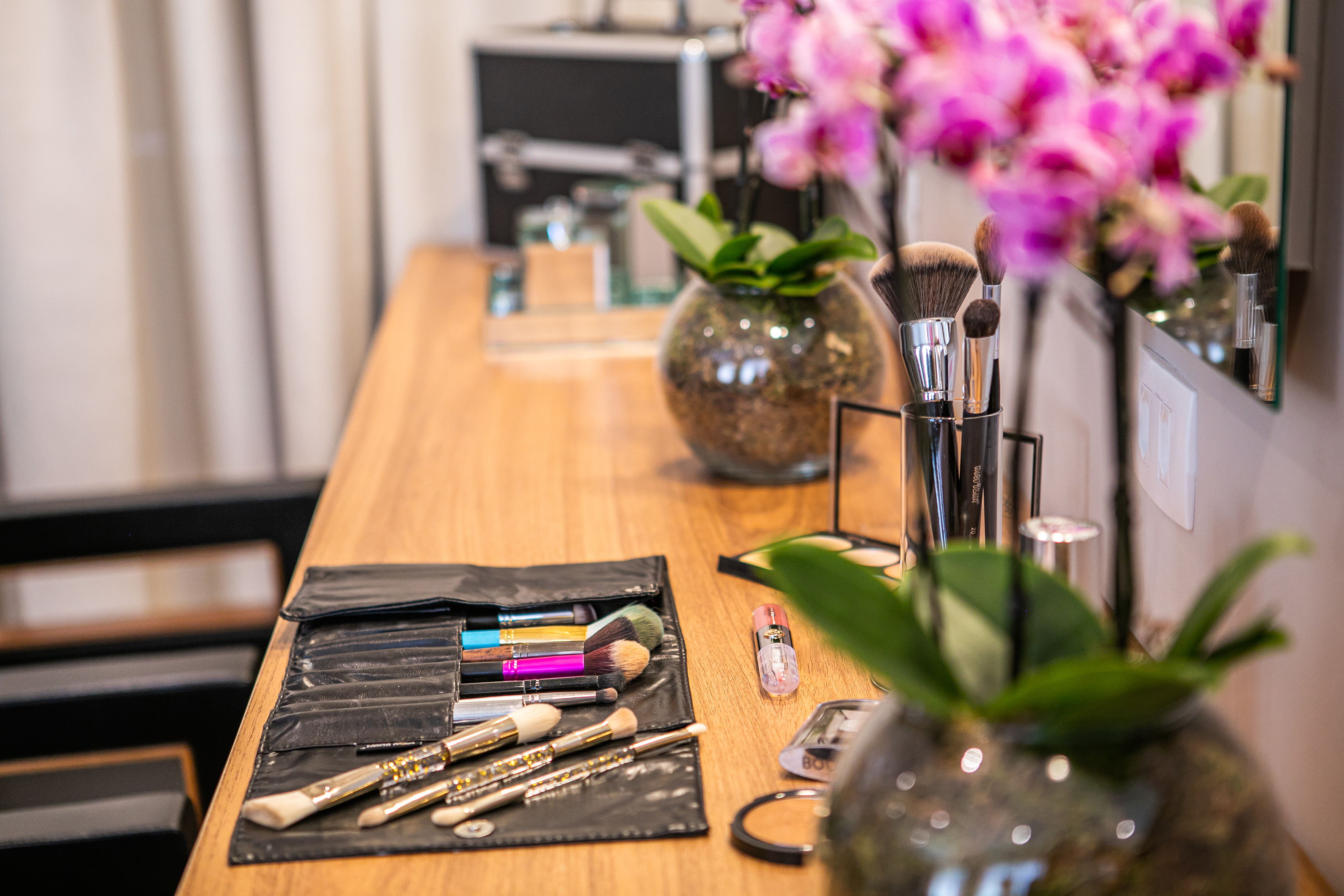 Professional makeup brushes and cosmetics on a wooden vanity with pink orchids.