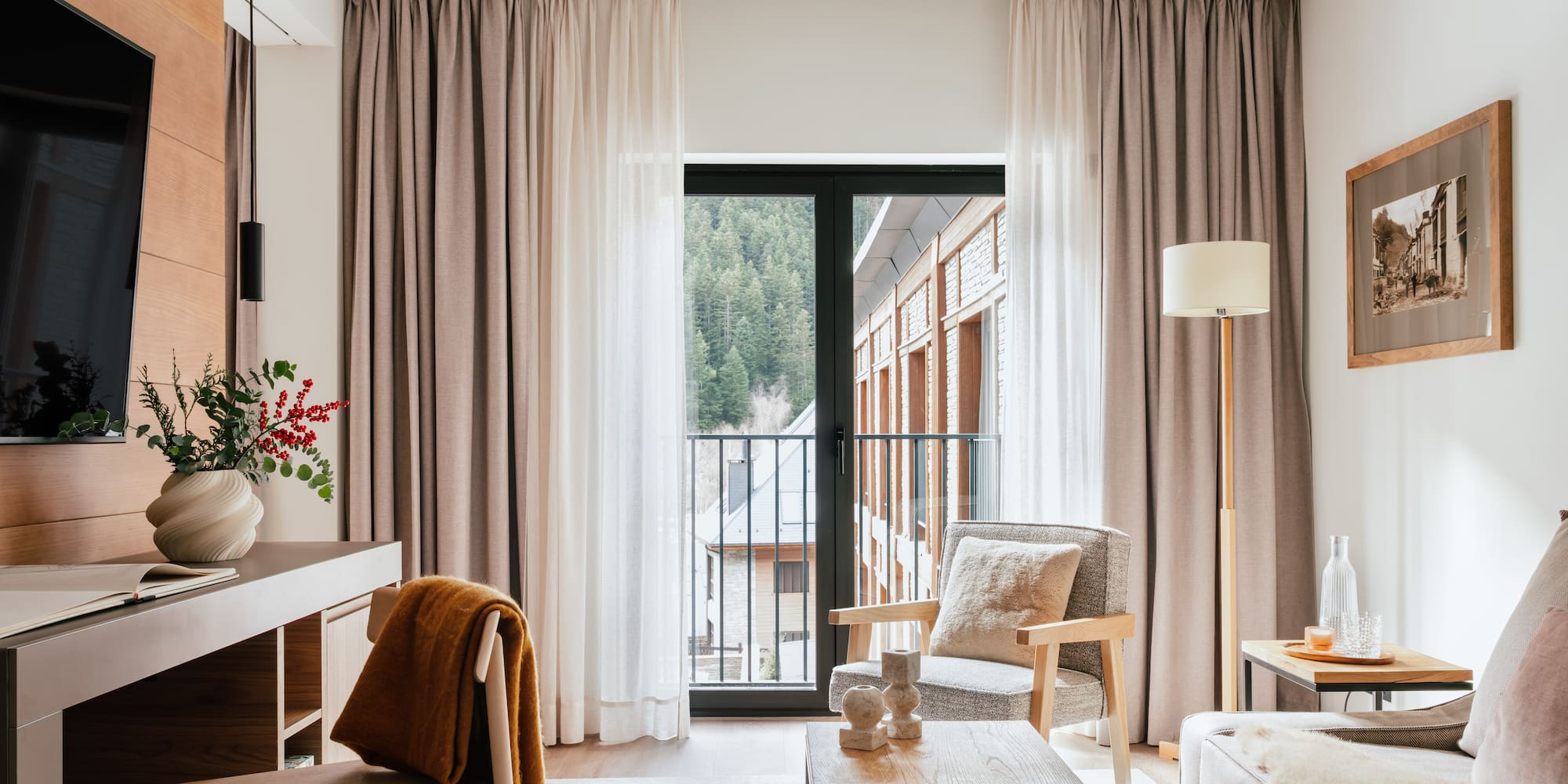 Cozy hotel suite living area with mountain view balcony, modern decor.