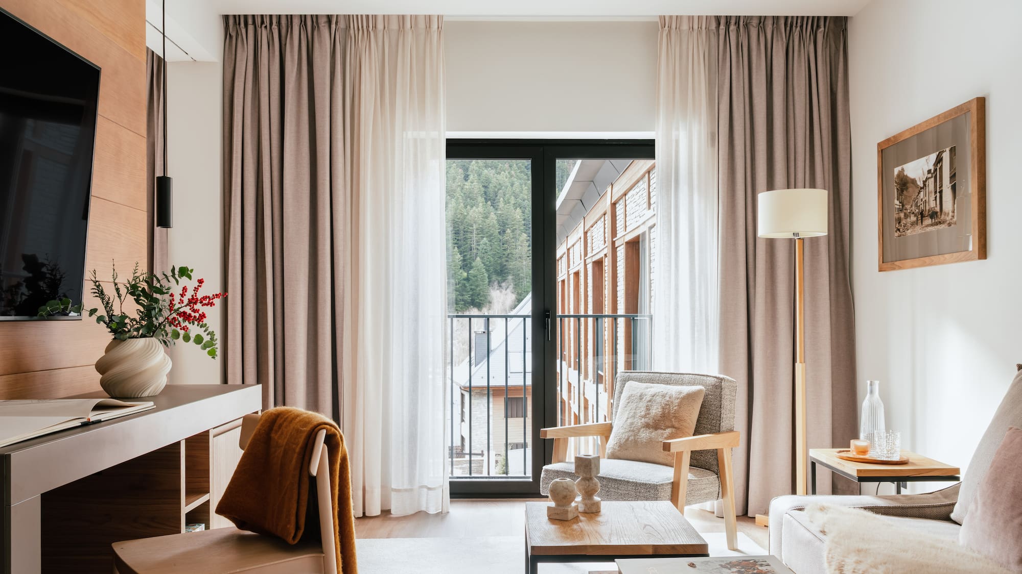 Cozy hotel suite living area with mountain view balcony, modern decor.