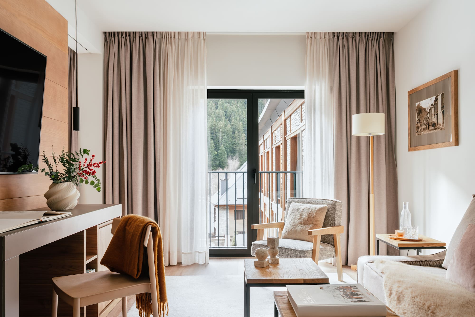 Cozy hotel suite living area with mountain view balcony, modern decor.