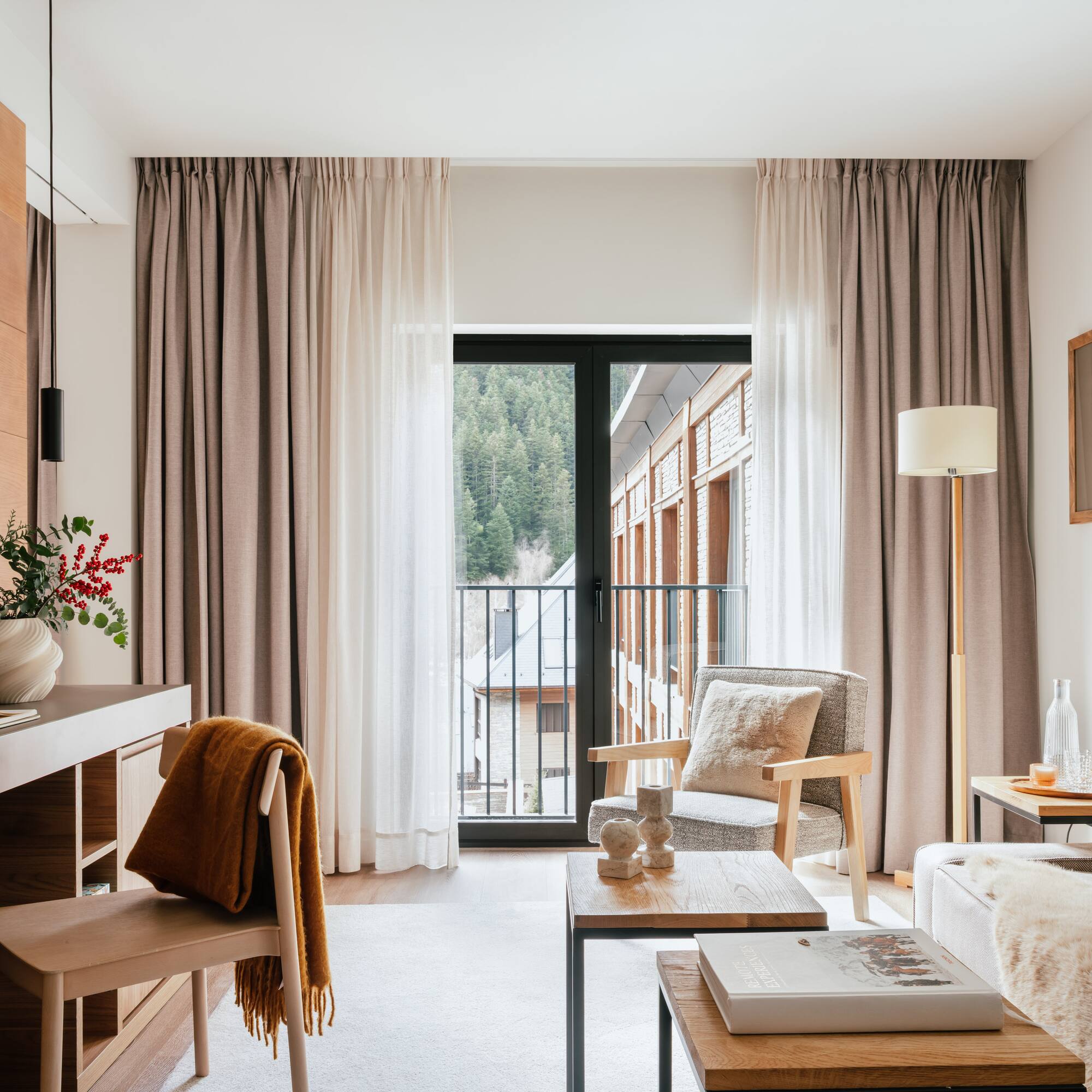 Cozy hotel suite living area with mountain view balcony, modern decor.