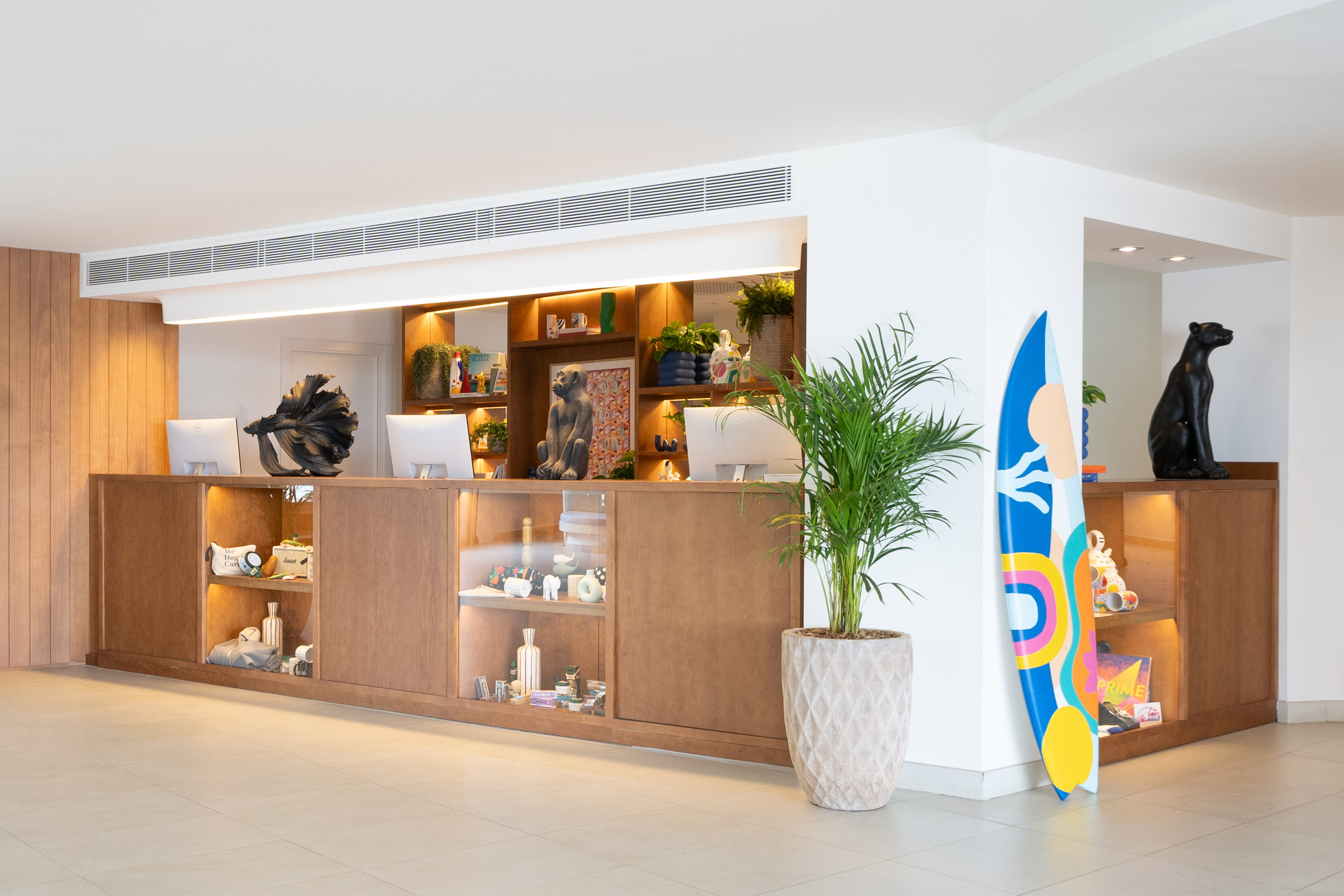 Contemporary hotel lobby reception with wooden desk, unique decor, and a colorful surfboard.