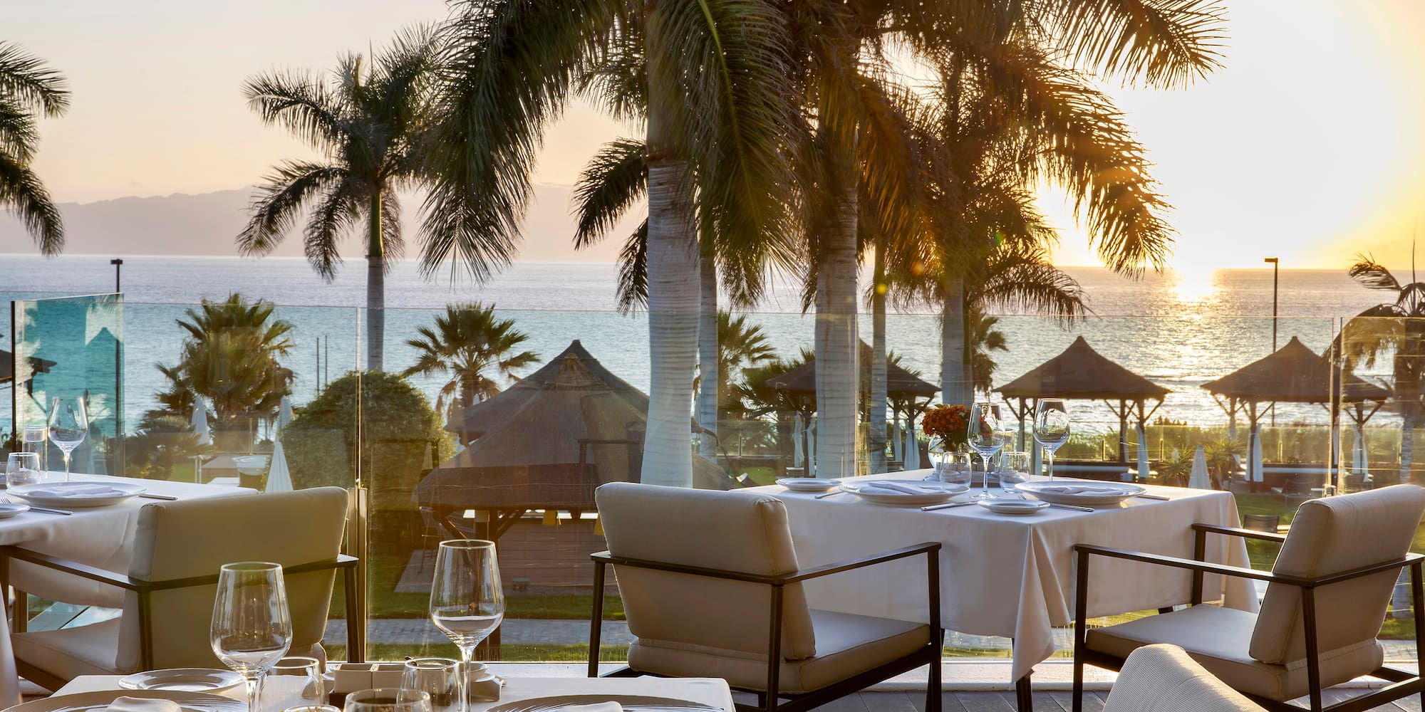 a table set for a dinner with palm trees and a beach in the background
