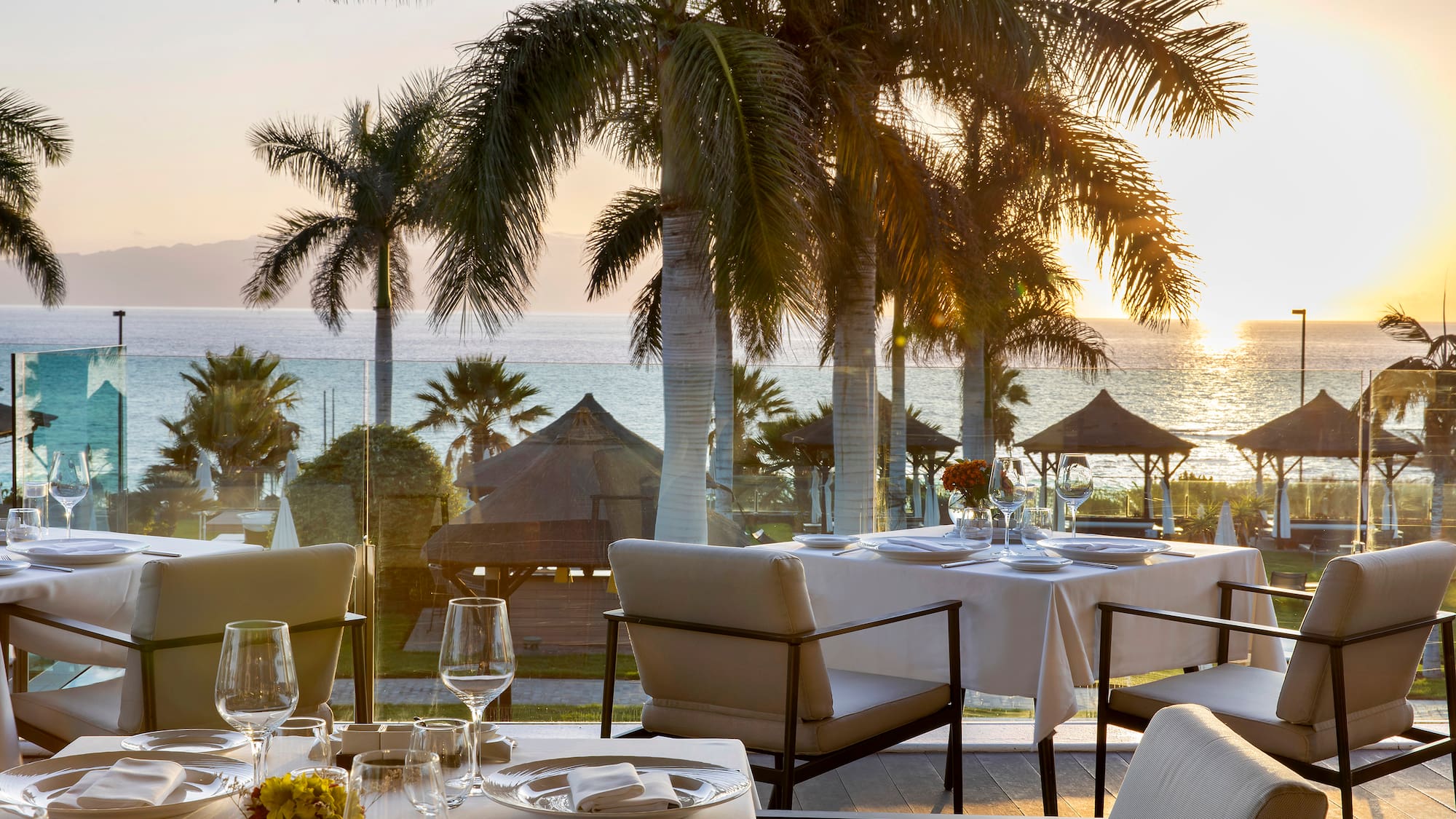 a table set for a dinner with palm trees and a beach in the background