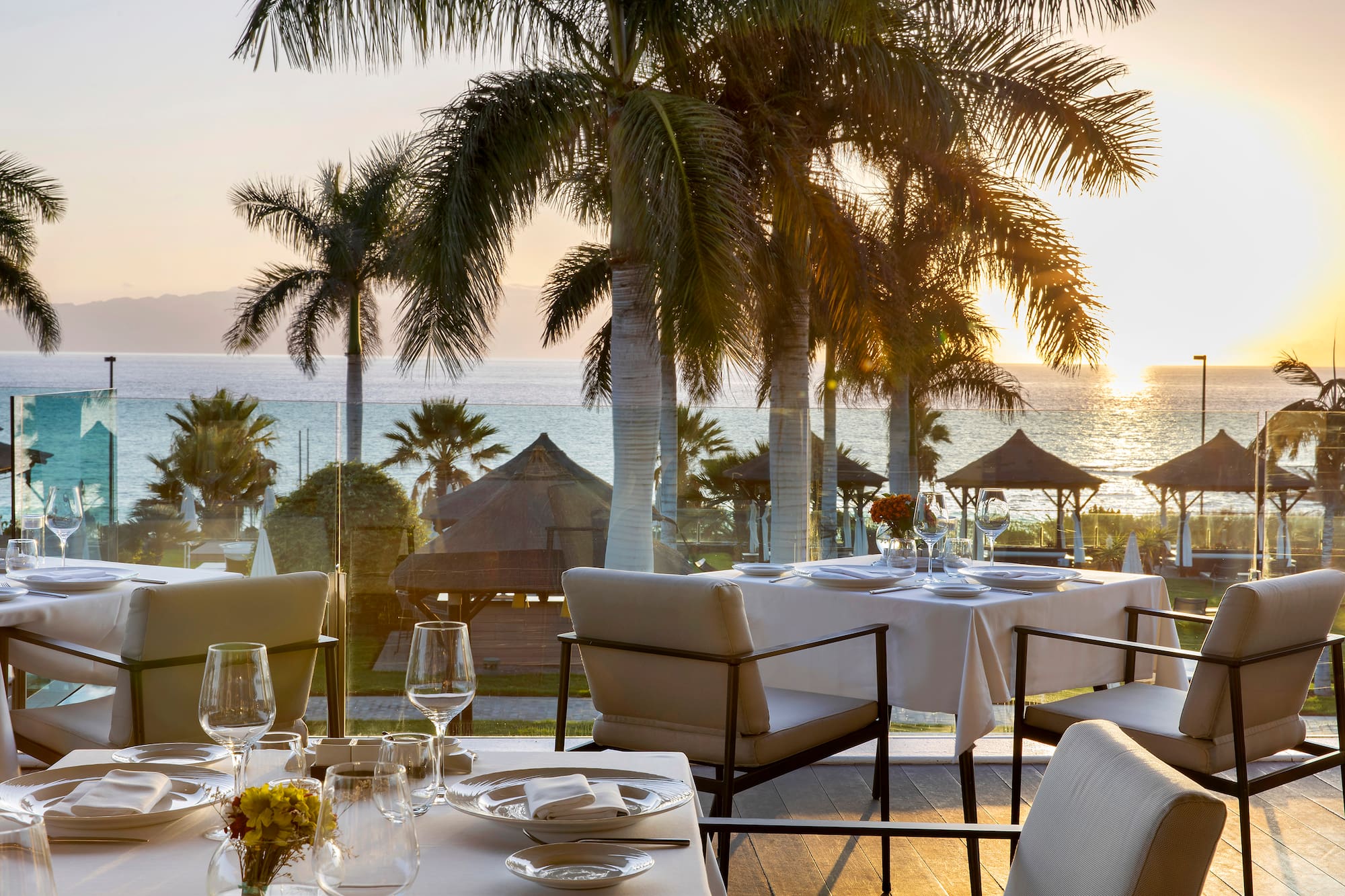 Elegant beachfront restaurant with palm trees, ocean view, and sunset.