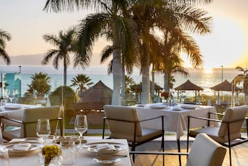 a table set for a dinner with palm trees and a beach in the background