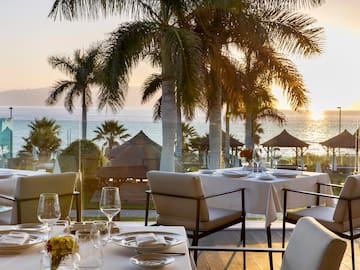 a table set for a dinner with palm trees and a beach in the background